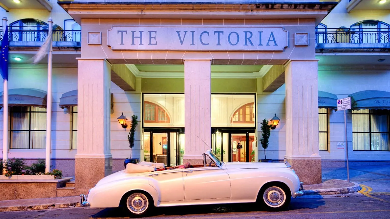 The entrance of AX The Victoria in Sliema at dusk, with a vintage car outside
