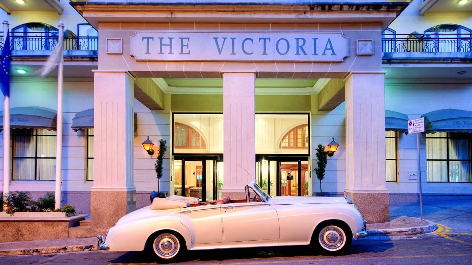 The entrance of AX The Victoria in Sliema at dusk, with a vintage car outside