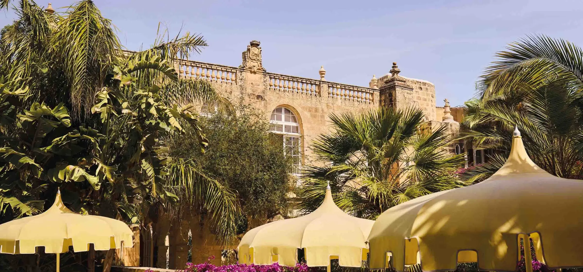 The garden of Casa Bonavita, palms and white canopies before the house’s stone façade