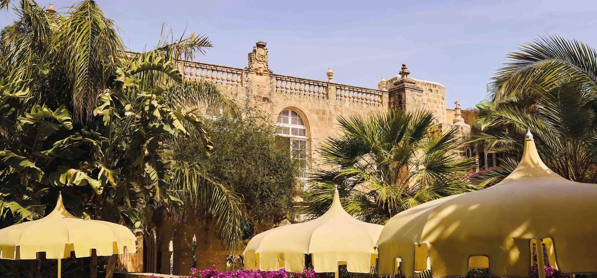 The garden of Casa Bonavita, palms and white canopies before the house’s stone façade