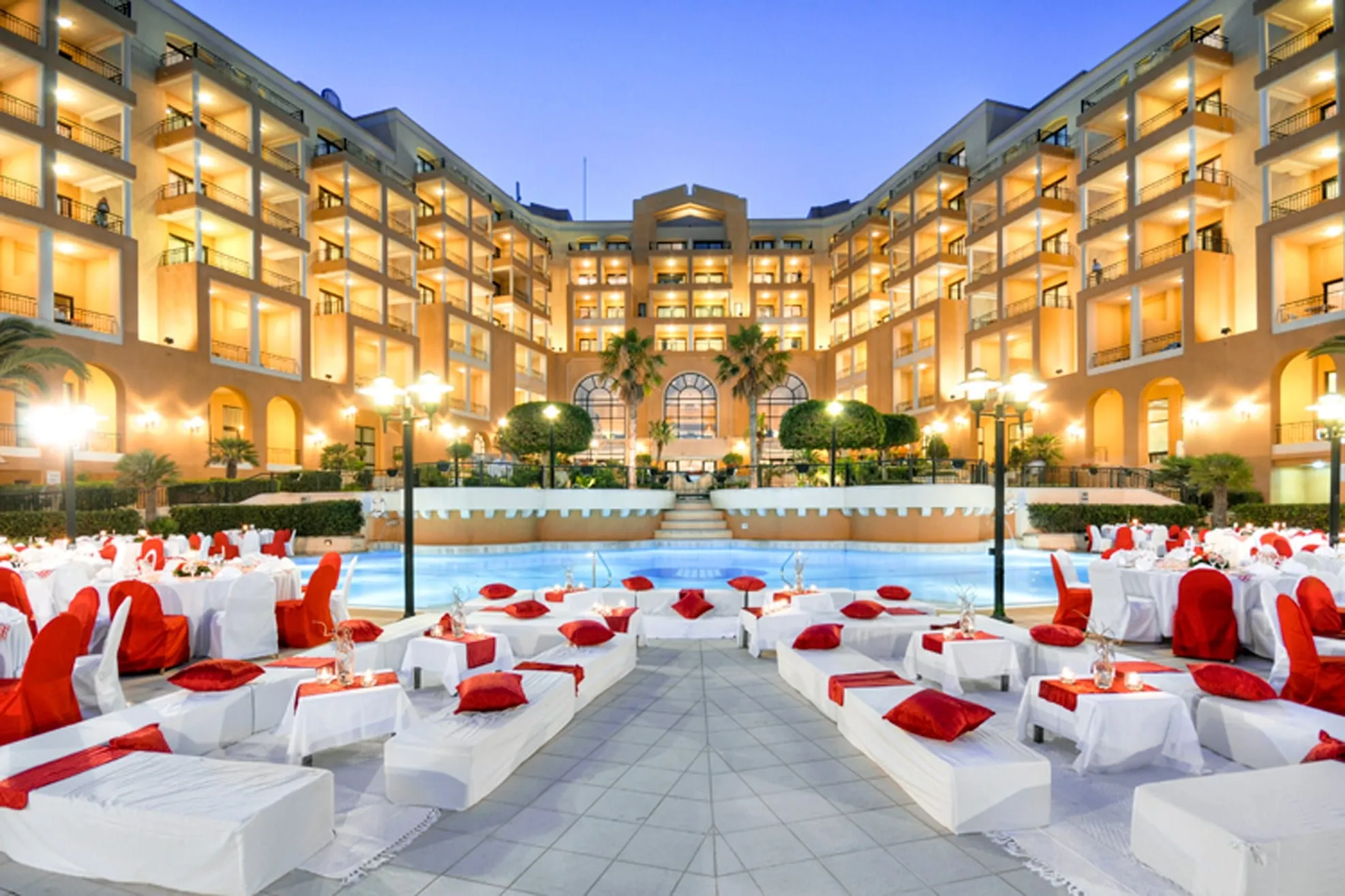 Corinthia St George's Bay lit at dusk, with tables set for an outdoor dinner around the pool