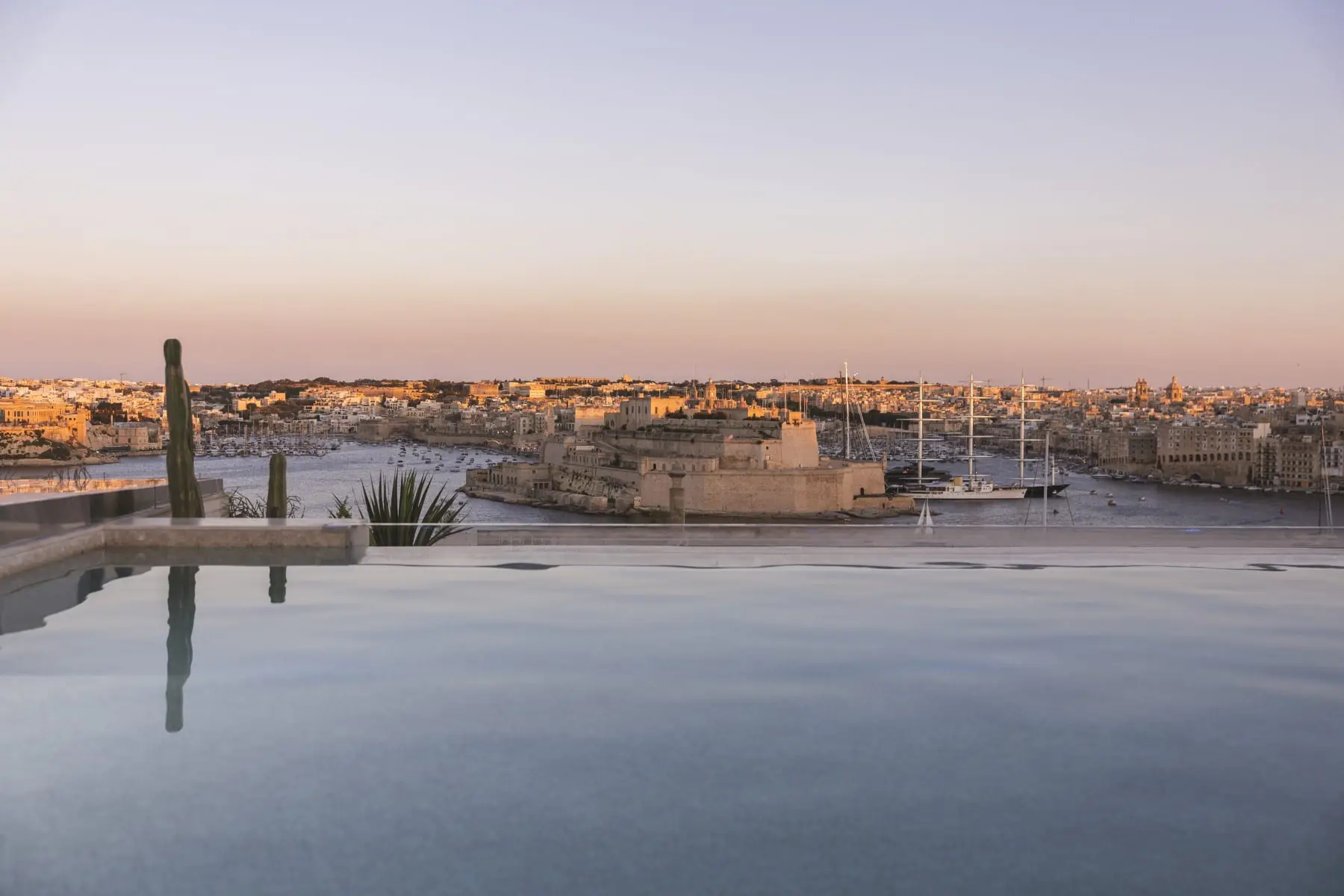 The rooftop infinity pool at dusk, looking across the Grand Harbour to Fort St Angelo and Birgu