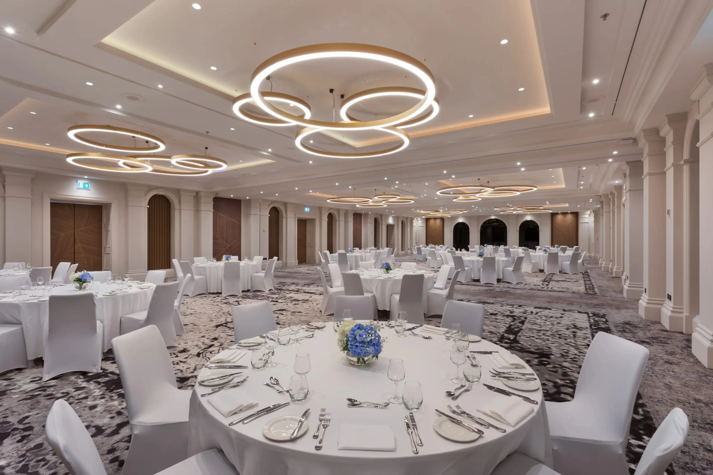 The Hilton Malta’s ballroom set with round tables under its ring chandeliers