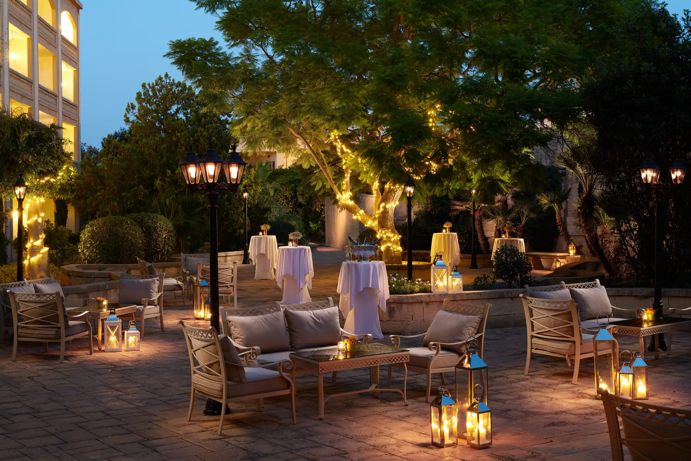 The Caprice Garden at dusk, with lounge seating, lanterns and tables set for a reception