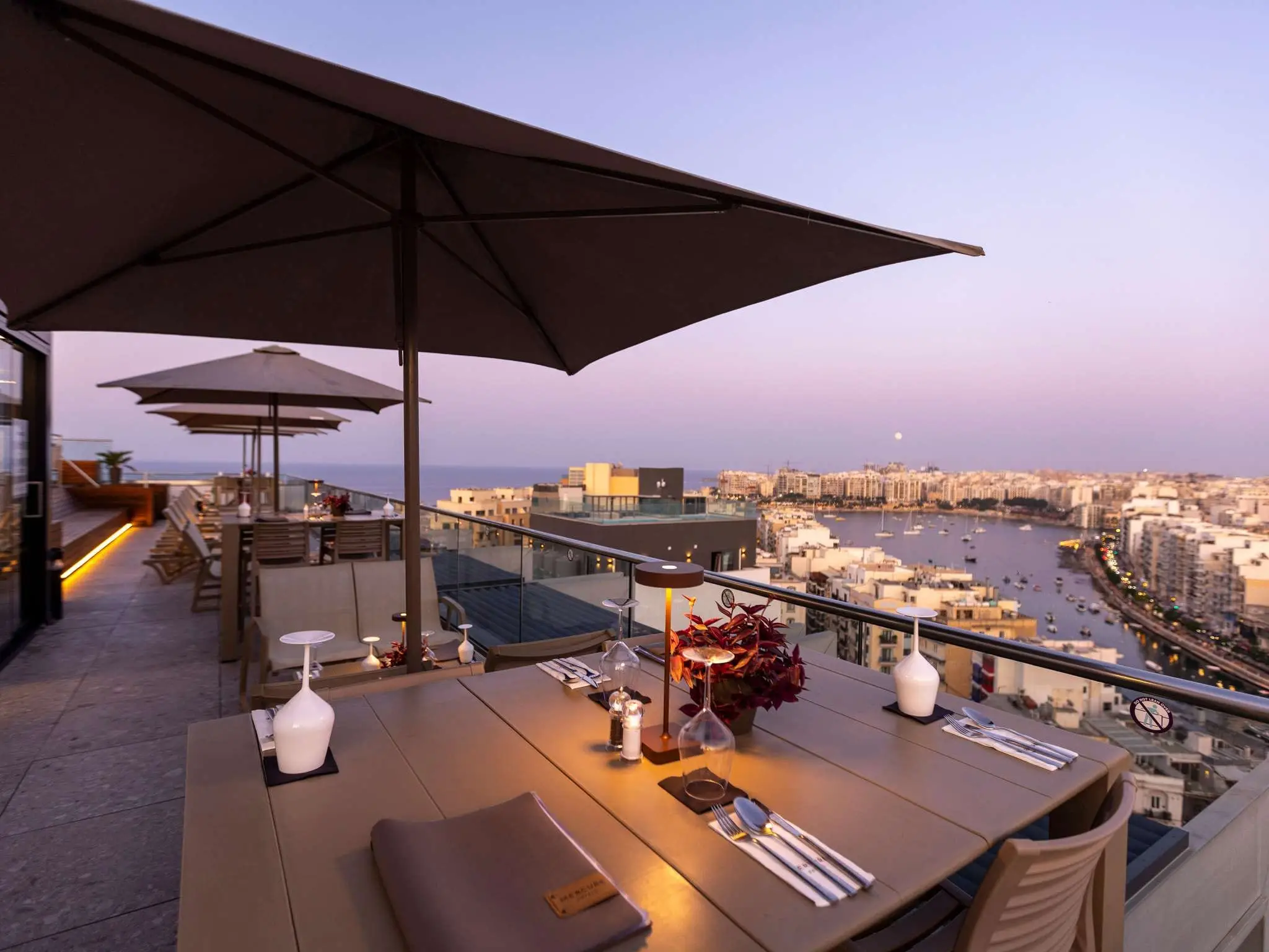Tables set on the Mercure St Julian’s rooftop terrace at dusk, above Spinola Bay