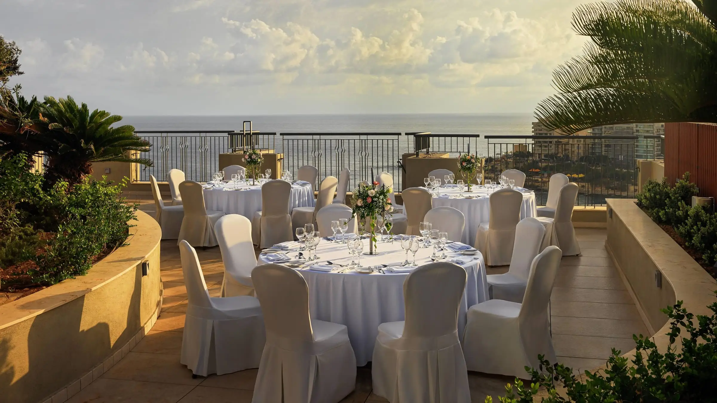 The Panoramic Terrace at the Malta Marriott set with round tables for dinner, with the sea beyond