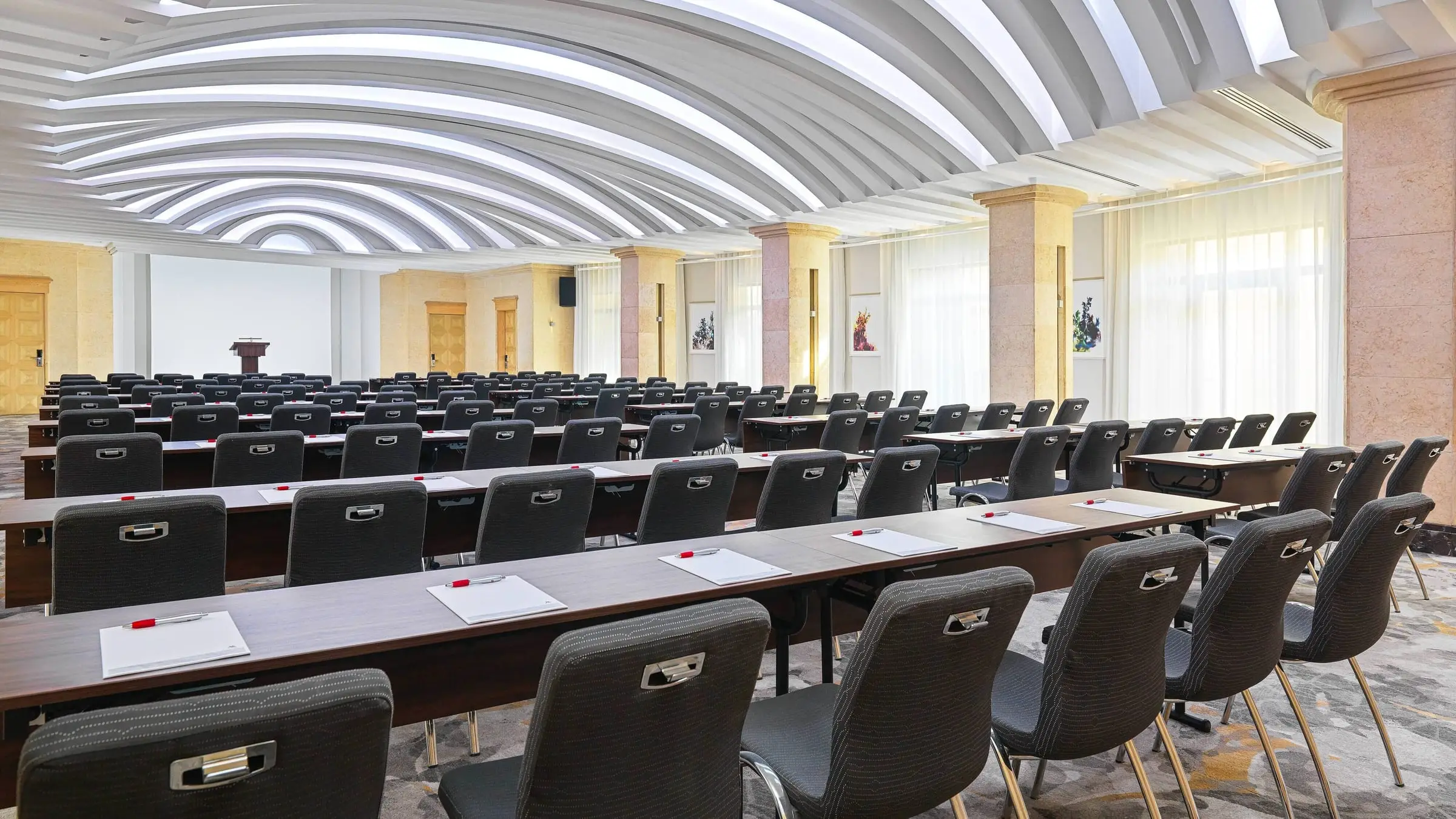 The ballroom at the Malta Marriott set classroom style, lit by tall windows