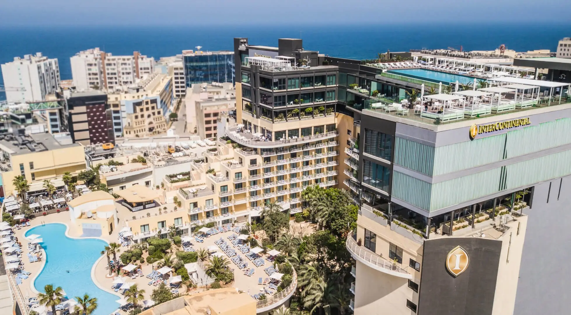 Aerial view of InterContinental Malta, its garden pool below and the rooftop pool above, with the sea beyond