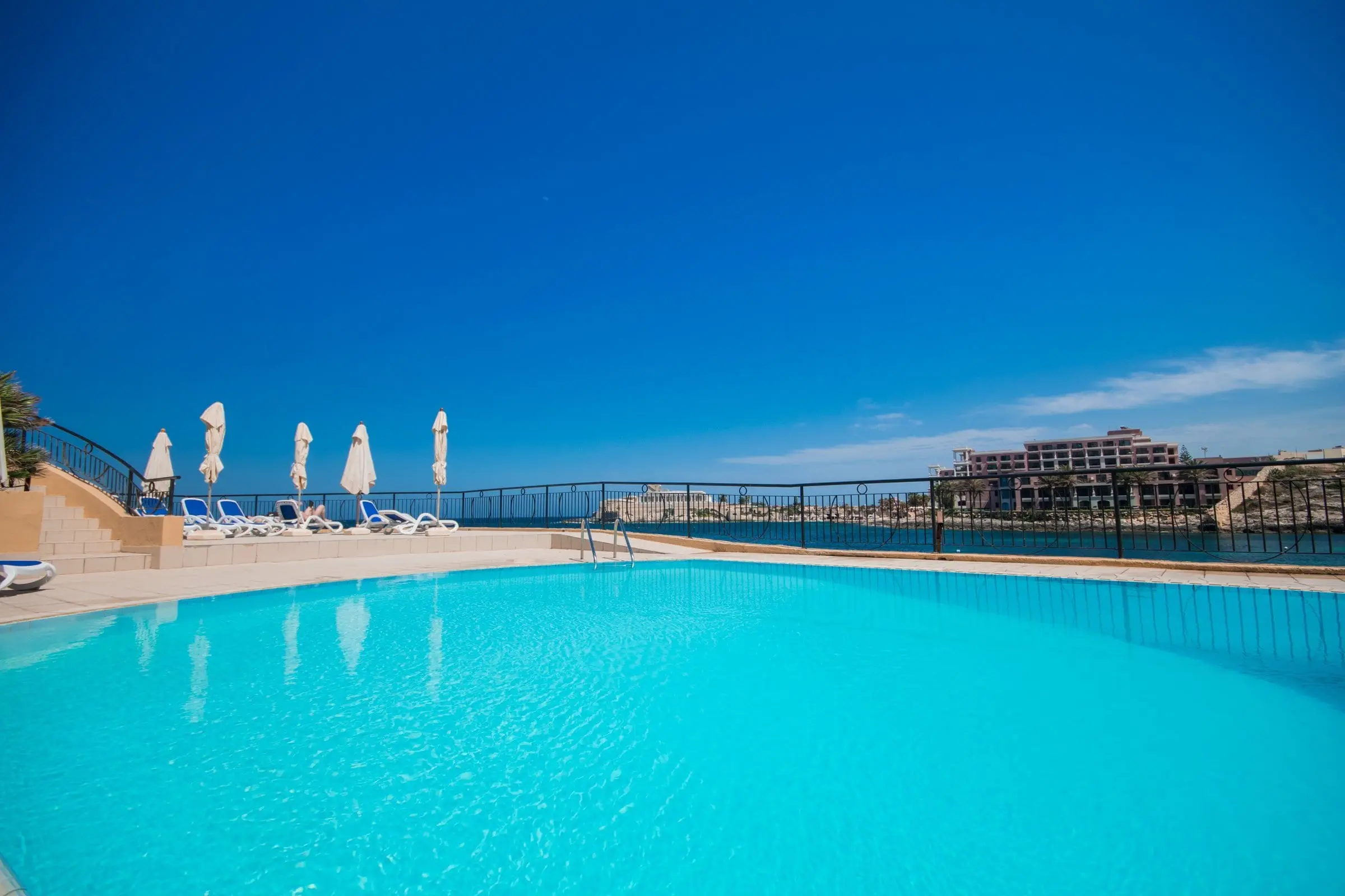 The hotel's outdoor pool beside the sea, looking across St George's Bay to Dragonara Point