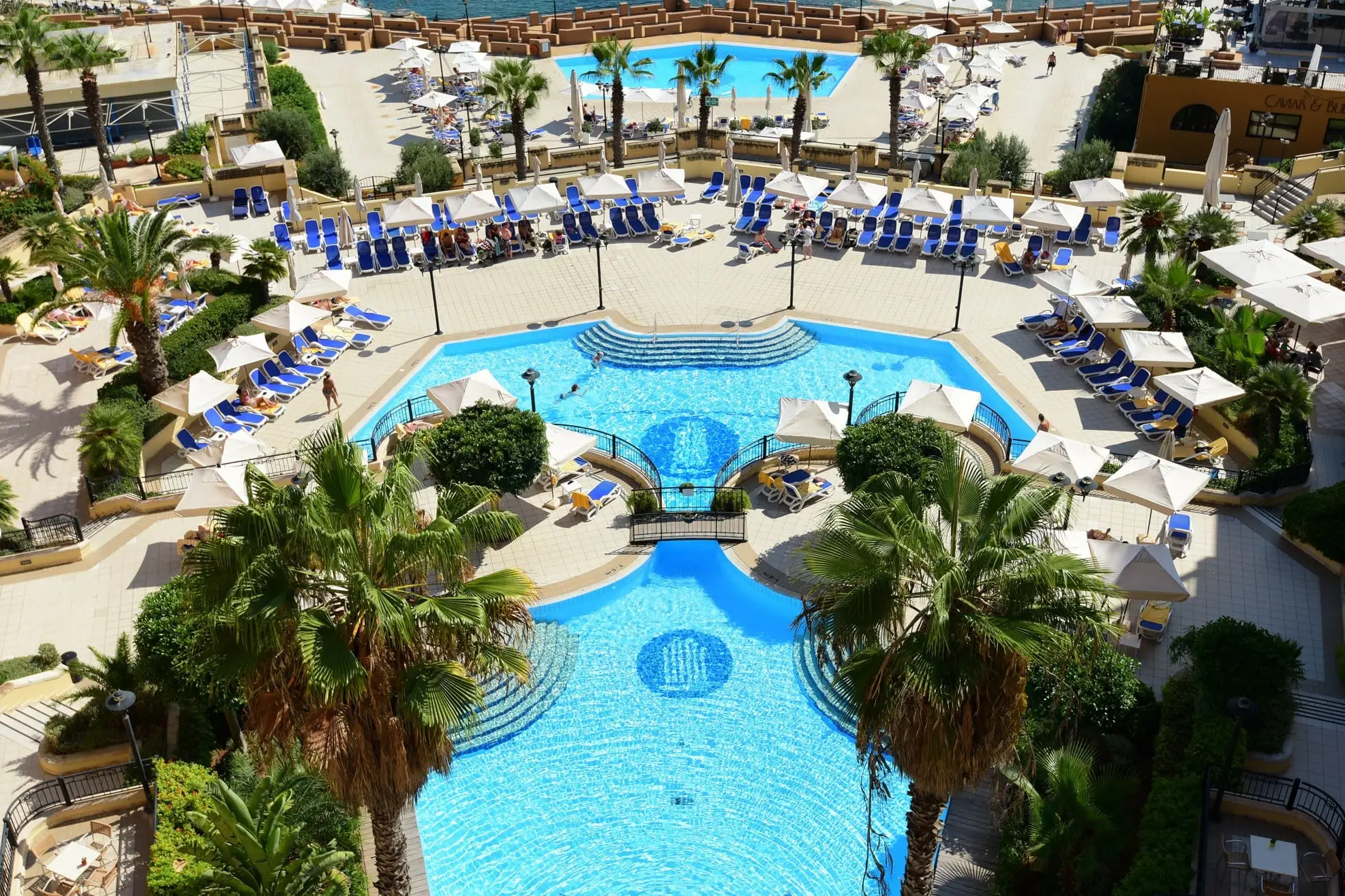 The hotel's outdoor pools seen from above, ringed by palms, parasols and loungers