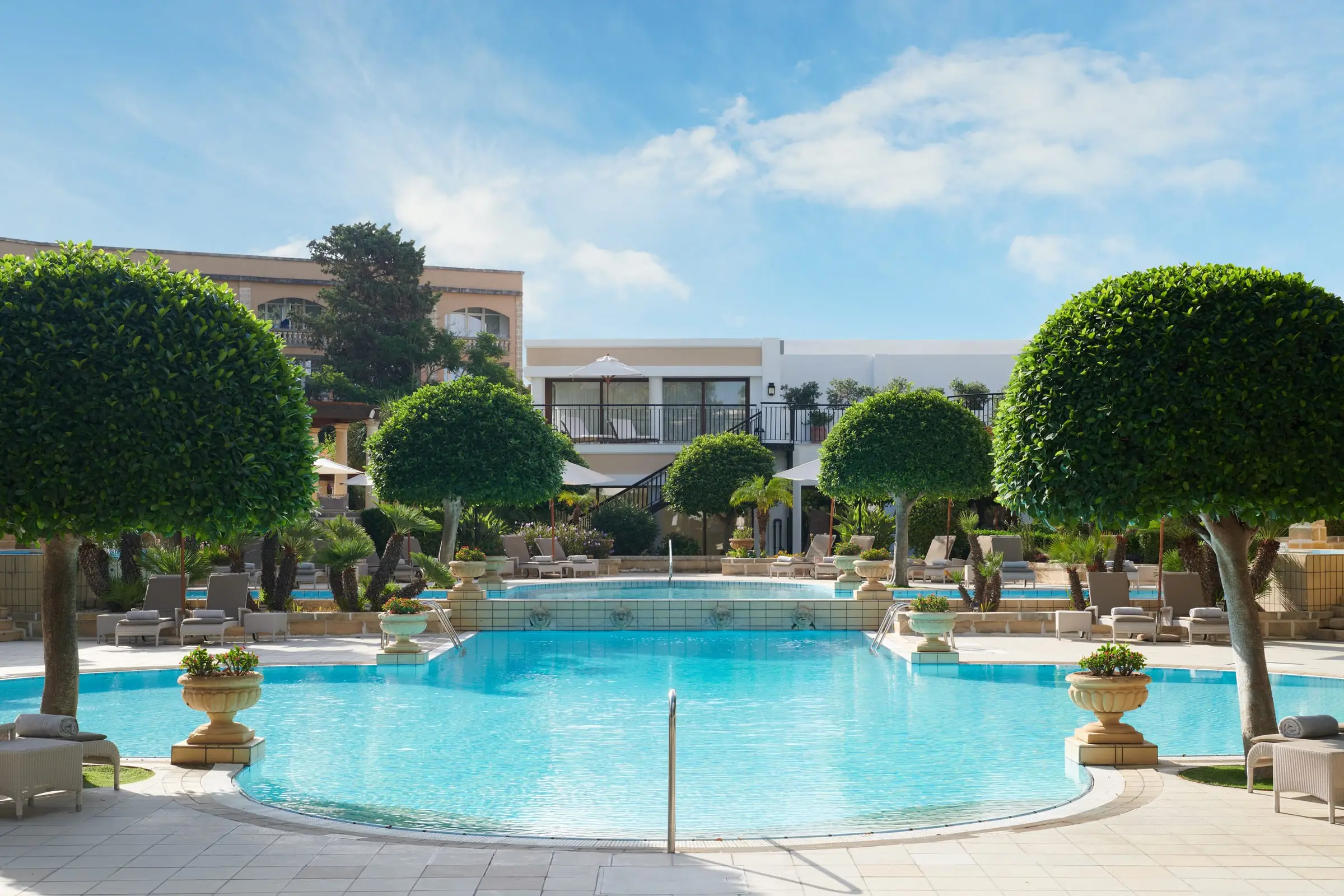 The outdoor pool in the hotel gardens, ringed by clipped trees and sun loungers