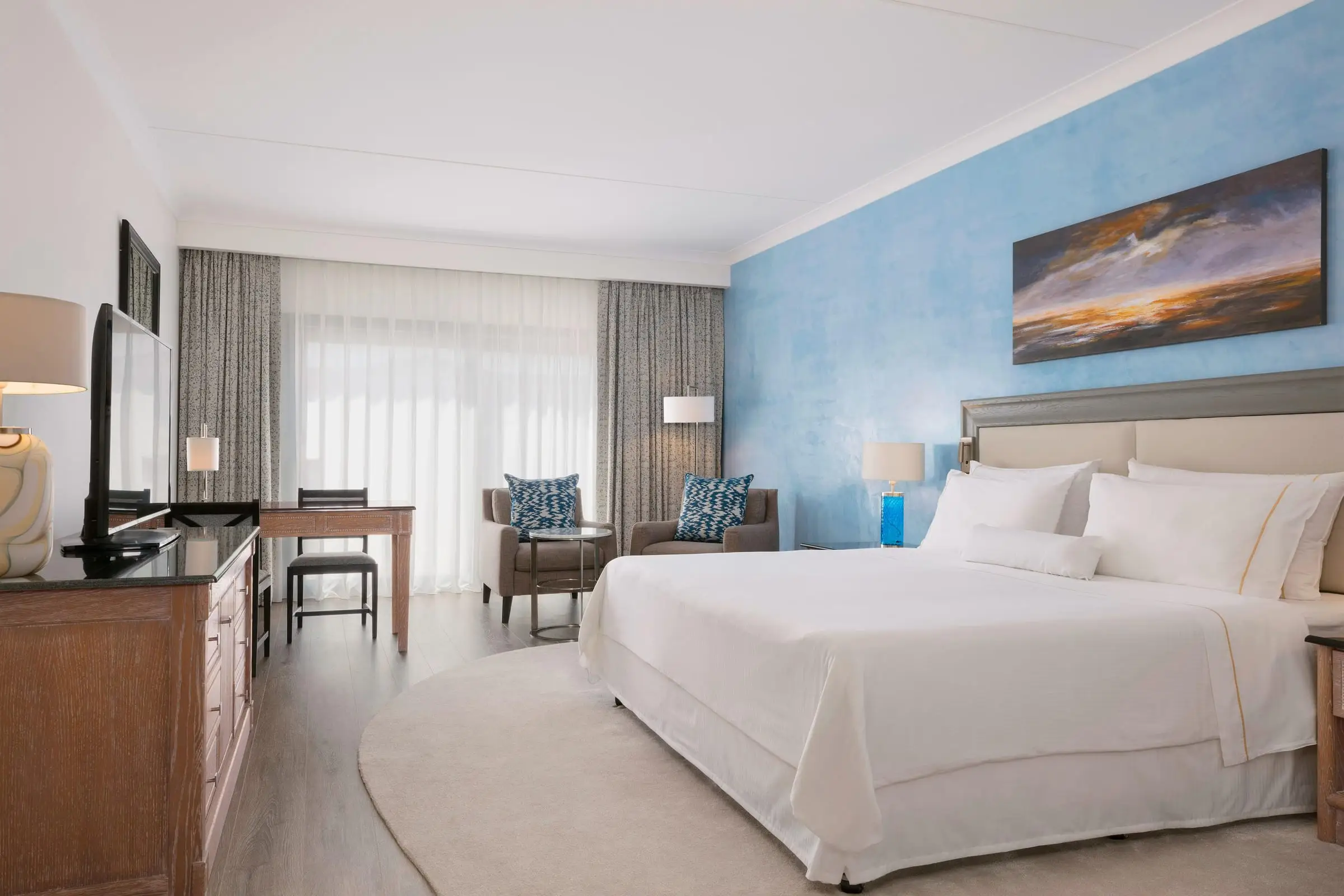 A king guest room with a blue feature wall and a seating corner by the window