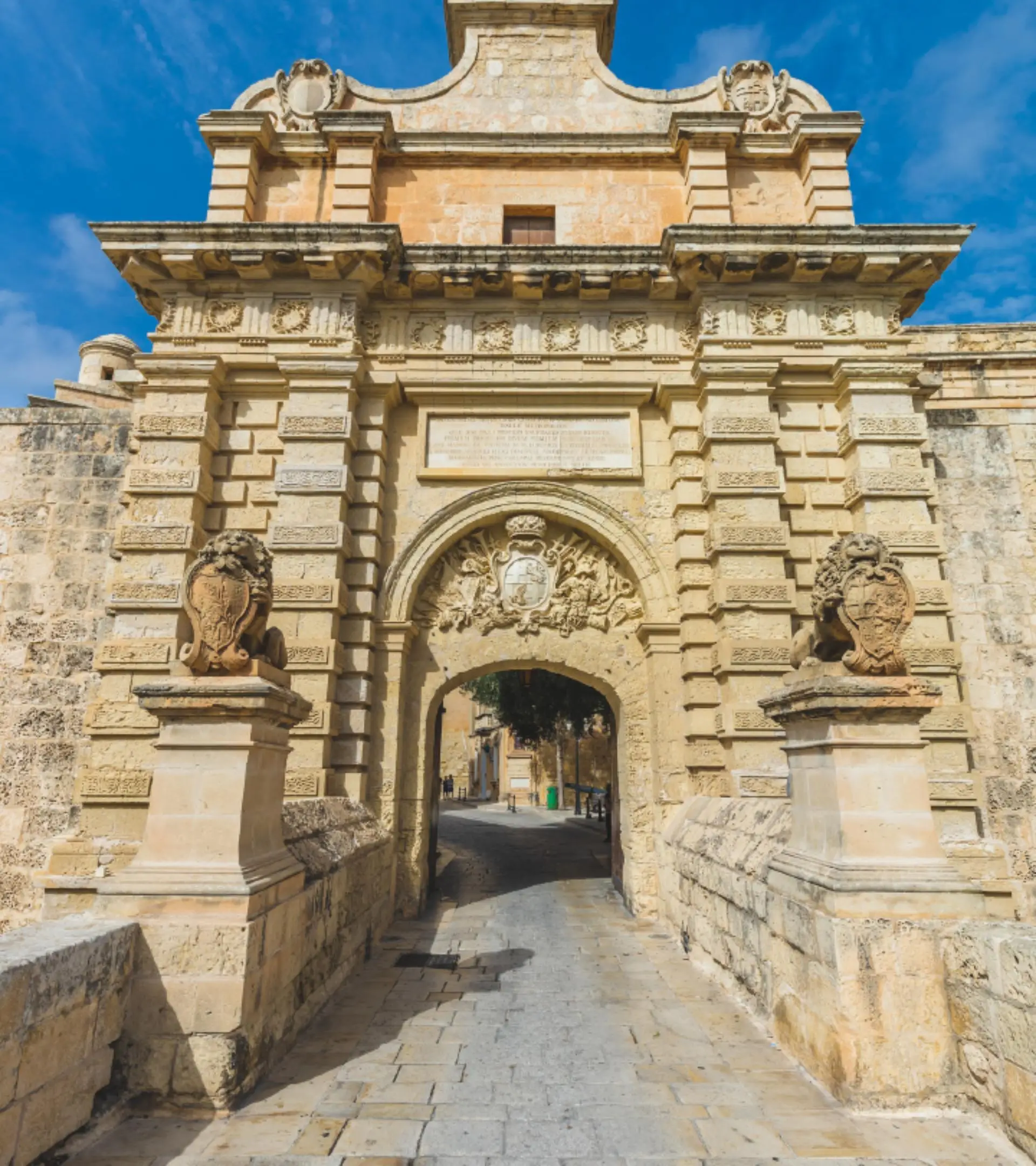 Mdina’s main gate, carved in Maltese limestone, the bridge leading in