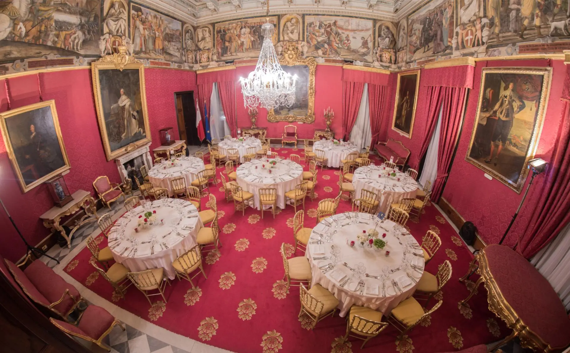 A red-walled state room set with round tables under a chandelier