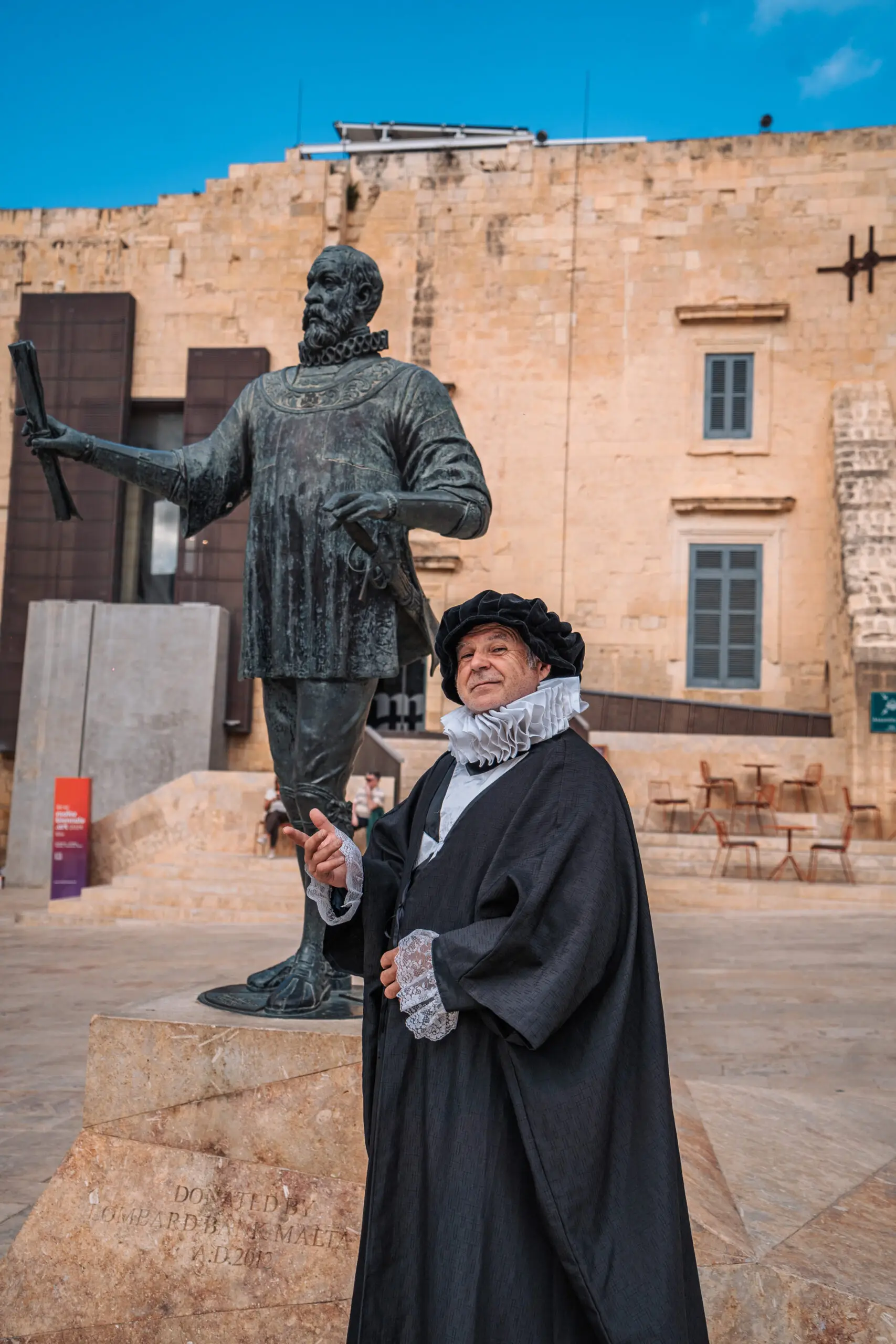 A costumed guide in character beside a bronze statue in a Valletta square
