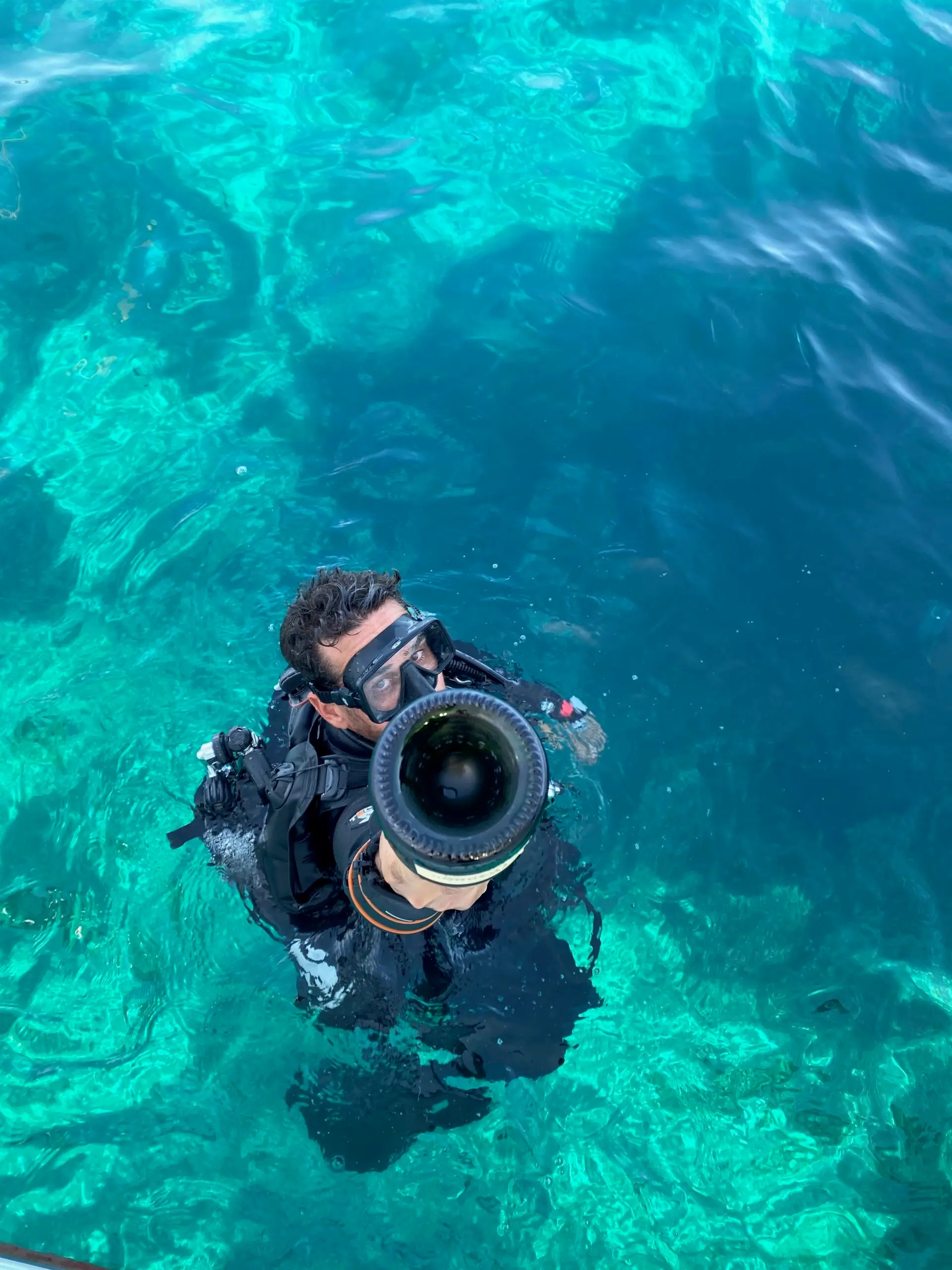 A diver with an underwater camera surfacing in clear turquoise water off the Maltese coast
