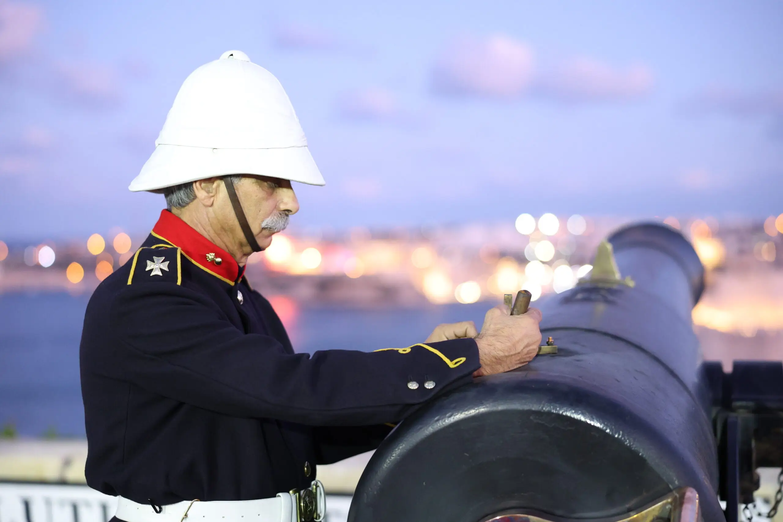 A gunner in ceremonial dress loading a cannon at the Saluting Battery at dusk