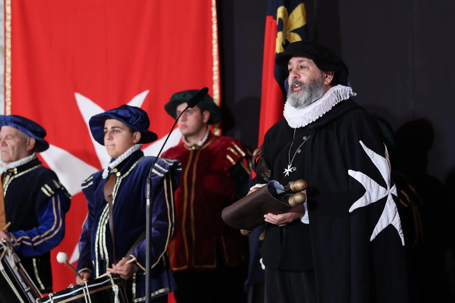 Costumed performers staged as the Knights of St John before a red backdrop