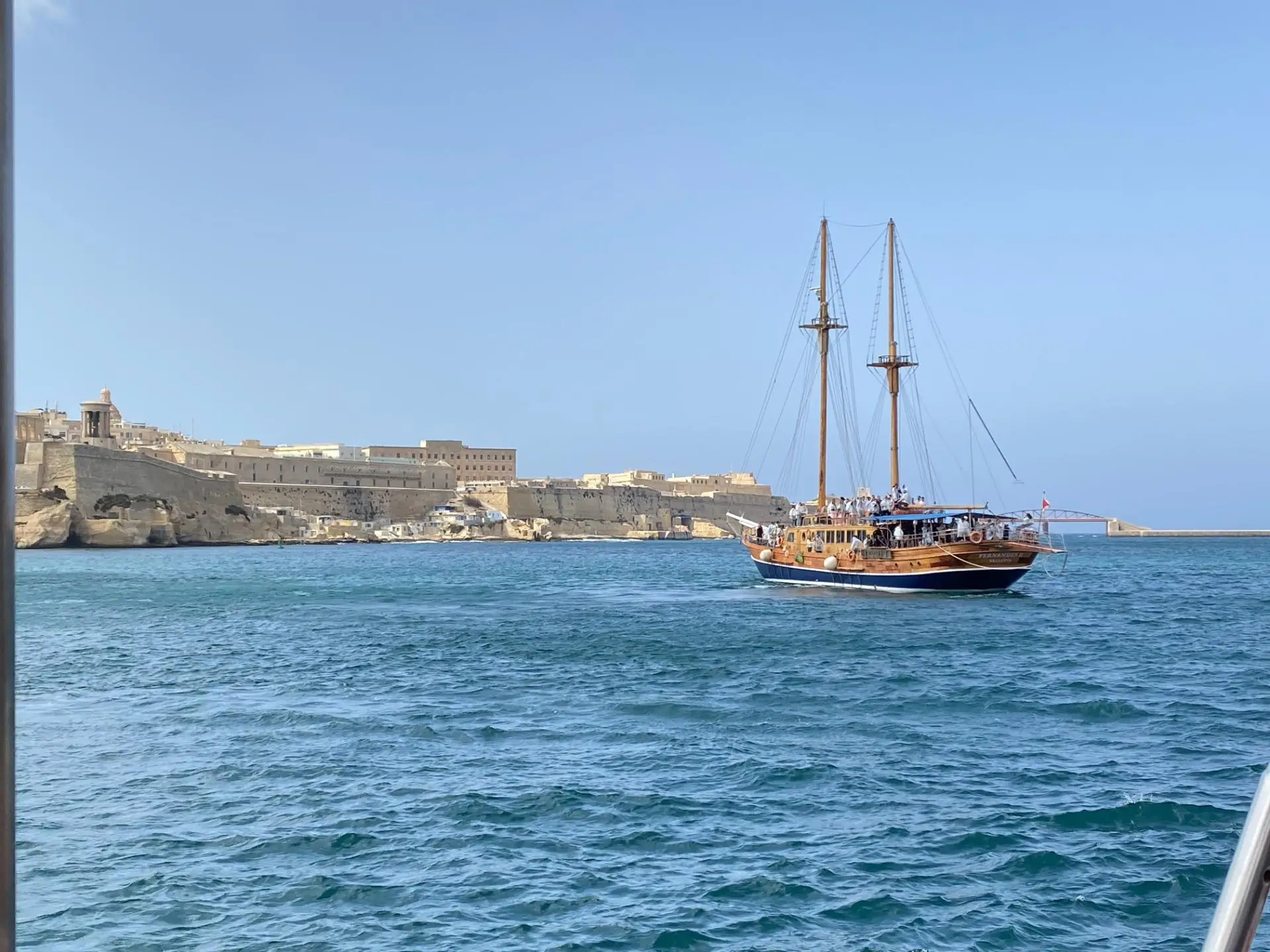 A two-masted schooner under sail off the Valletta bastions