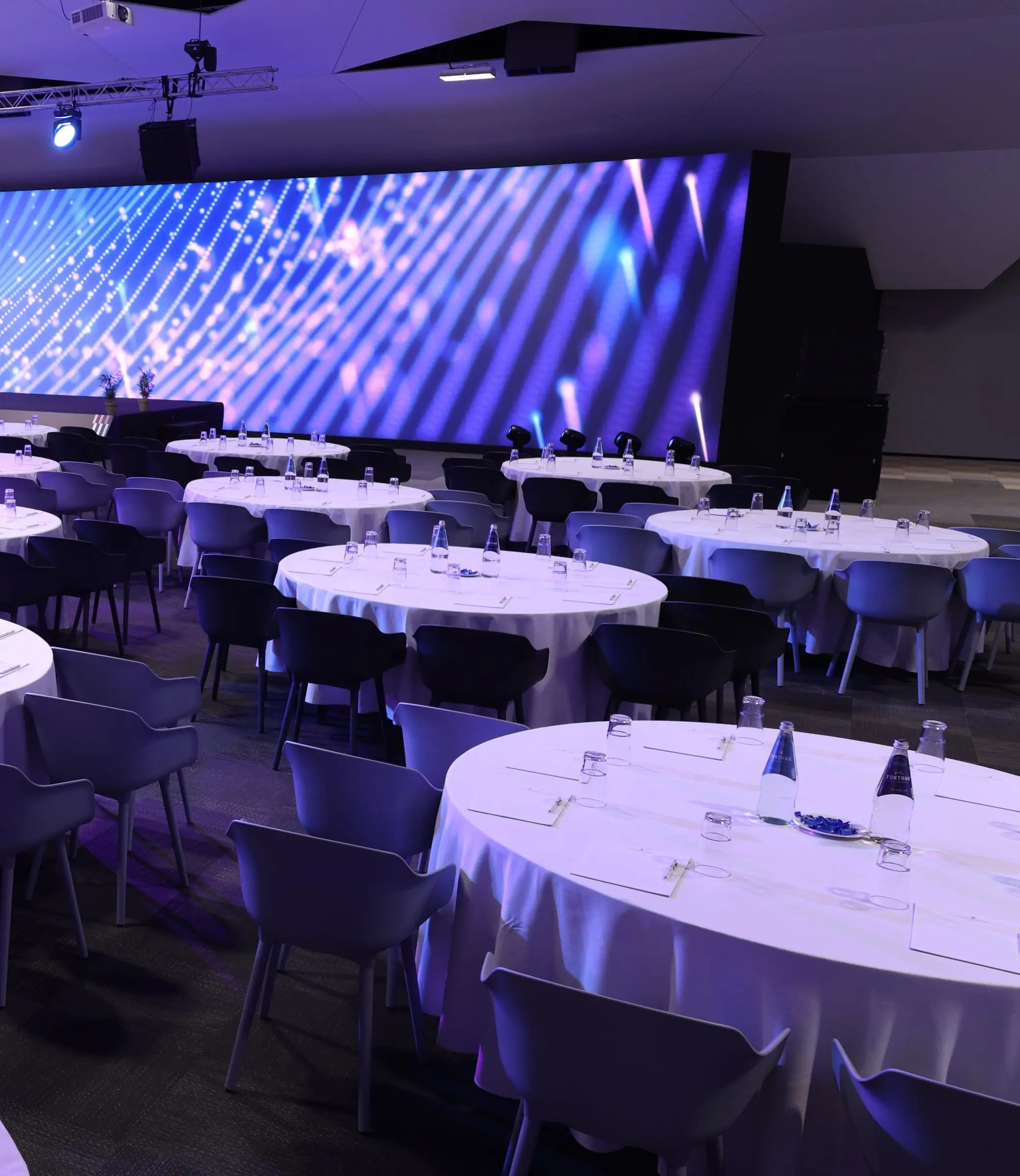 The resort arena set in cabaret rounds with white tablecloths and water bottles, facing a lit LED wall beneath the lighting rig