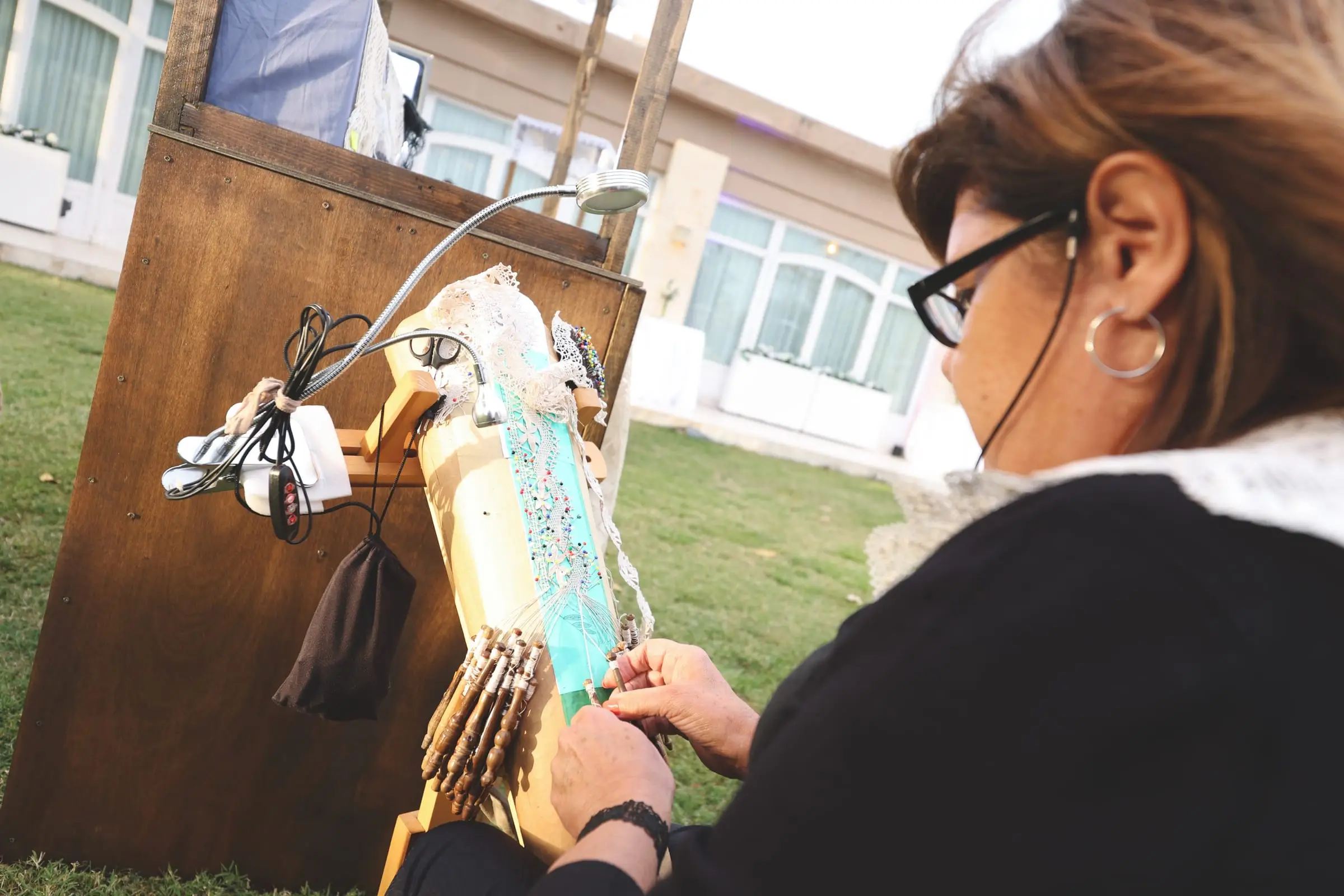 A lace-maker working bobbins on a lace pillow at her stall in the gardens