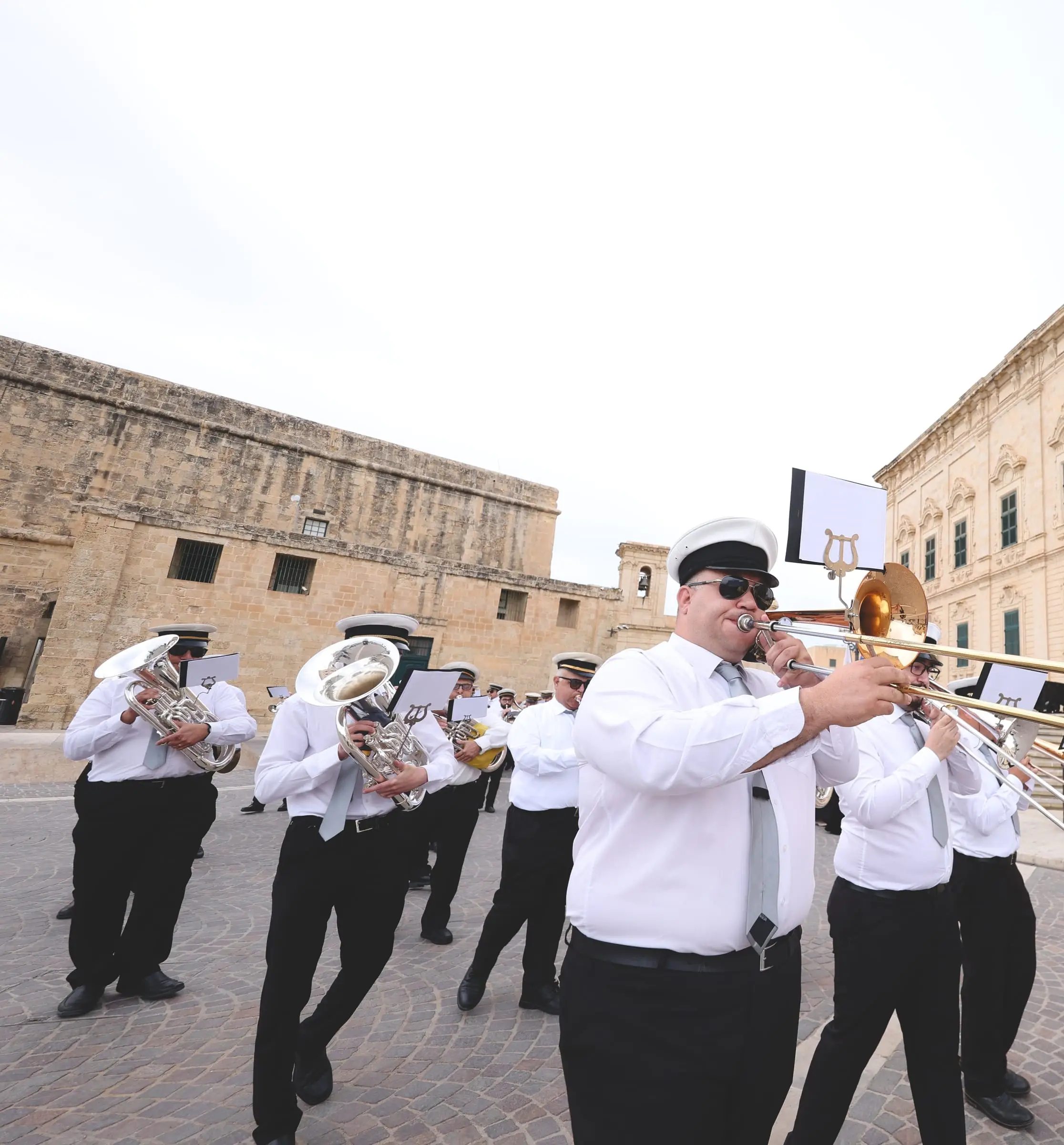 A trombonist leads the band across the square in front of the Auberge de Castille, its baroque façade and flags behind