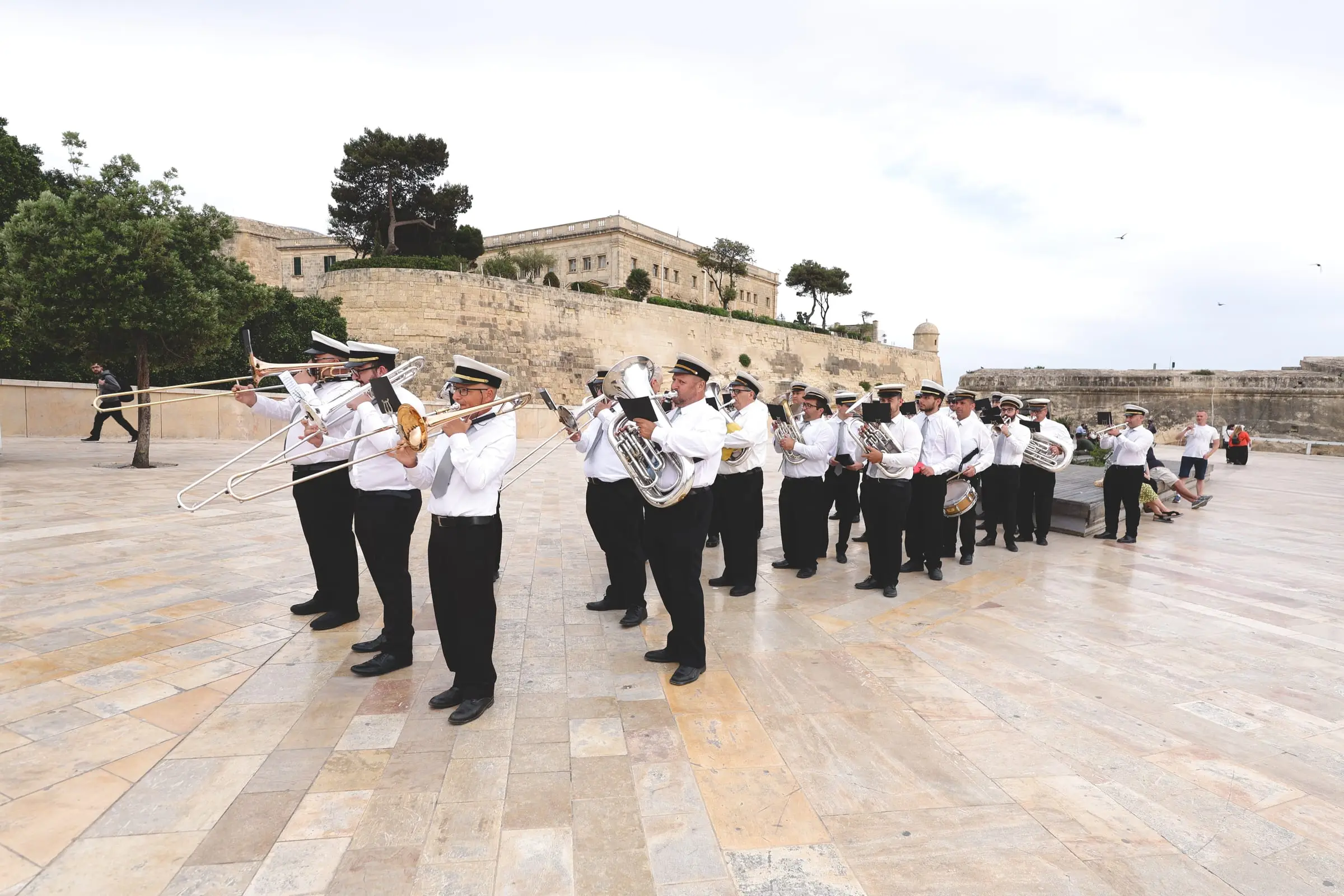 Trombones raised, the marching band in white shirts and peaked caps forms up on the stone square outside Valletta's bastions
