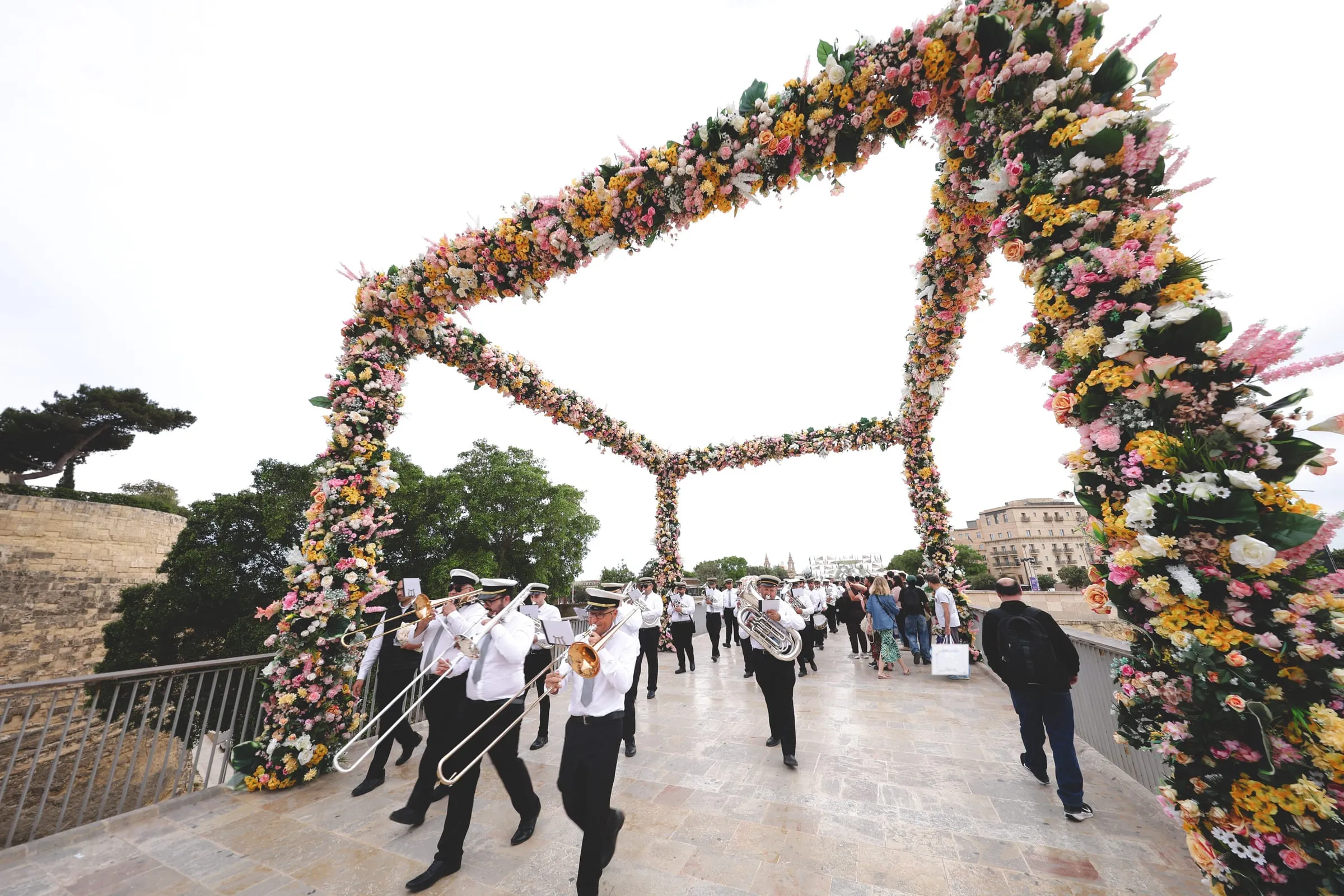 A marching band under an arch of flowers on the bridge into Valletta