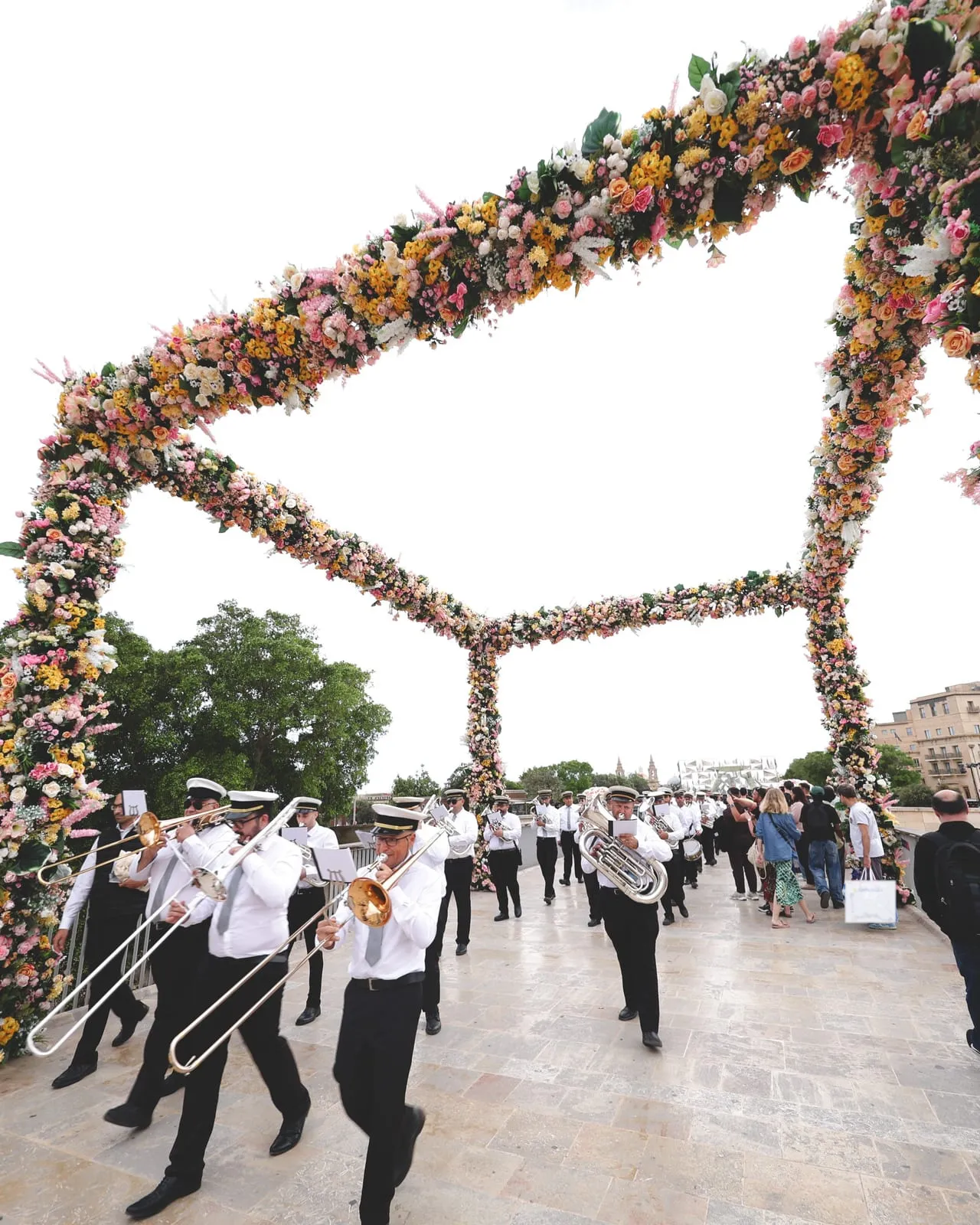 The marching band crosses the bridge into Valletta under an arch of flowers, trombones in front