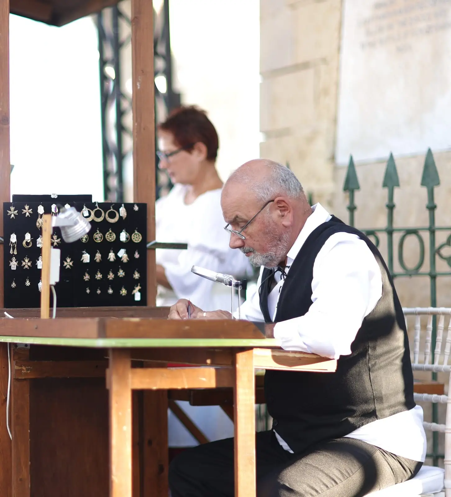 A silversmith at his bench beside a board of Maltese filigree crosses and pendants