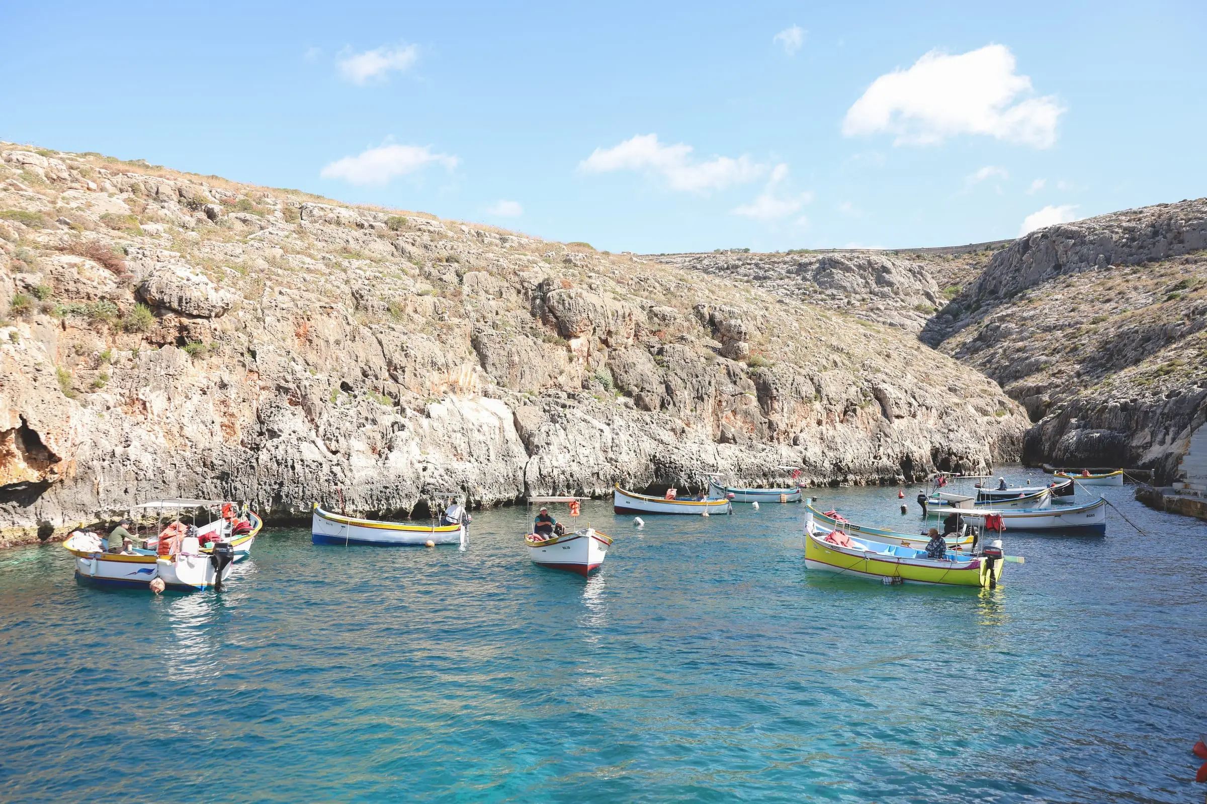 Painted wooden boats on turquoise water in the inlet below the cliffs at the Blue Grotto