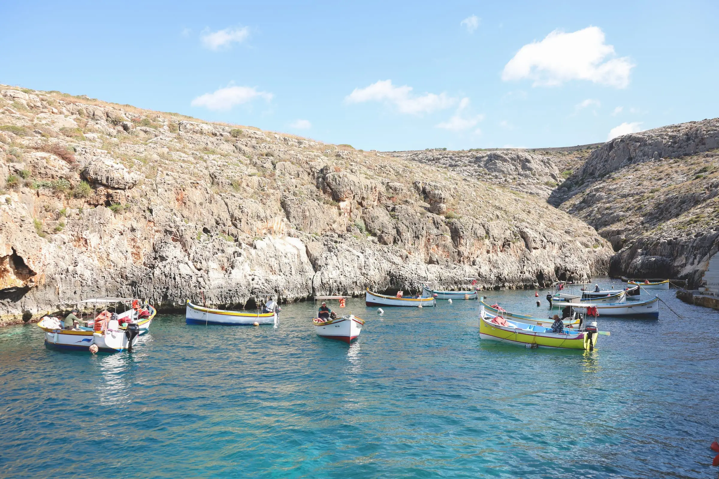 Painted wooden luzzu boats on clear water below the cliffs at the Blue Grotto