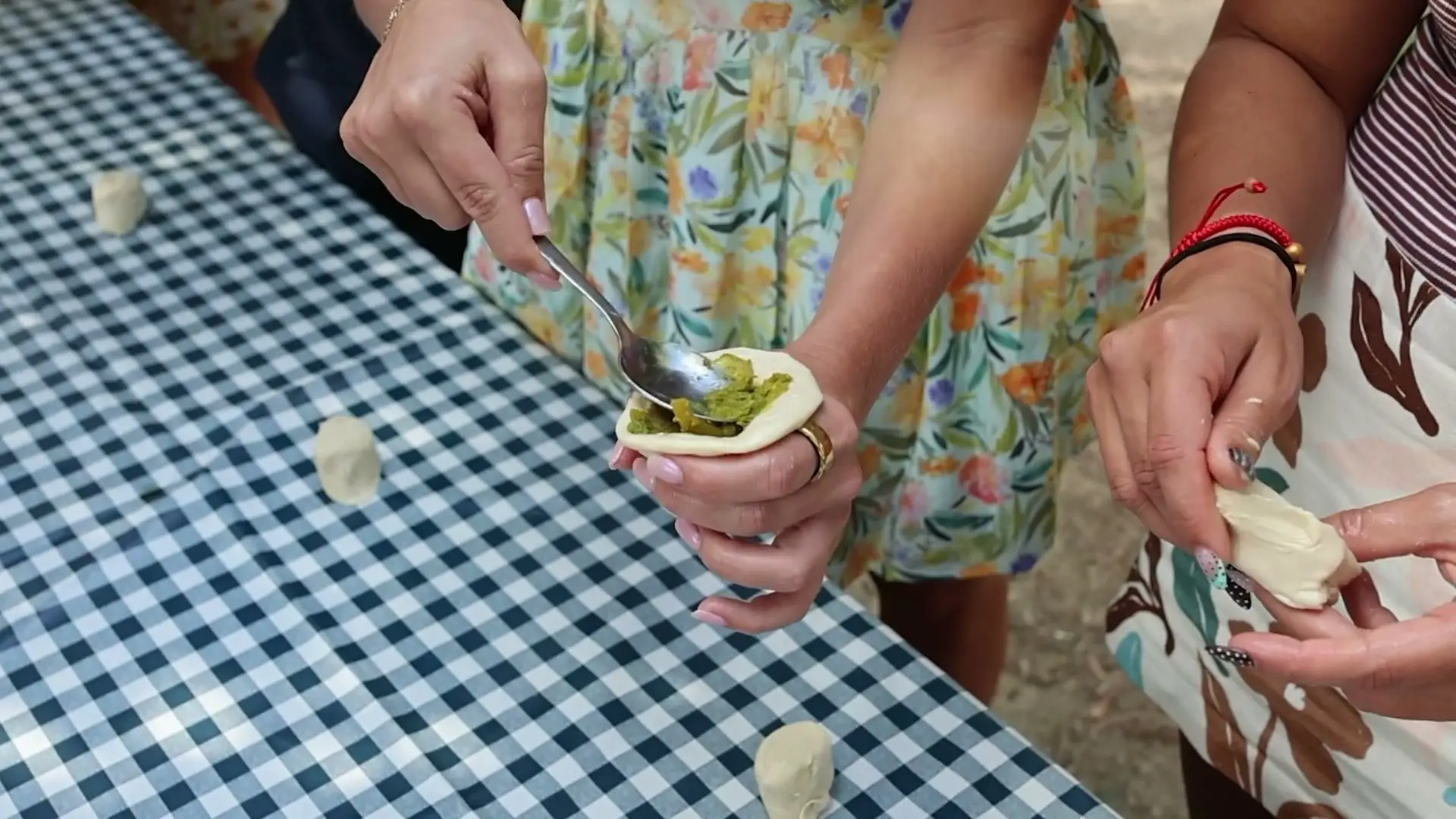 Hands filling pastry with a spoon over a gingham tablecloth at an outdoor cooking class