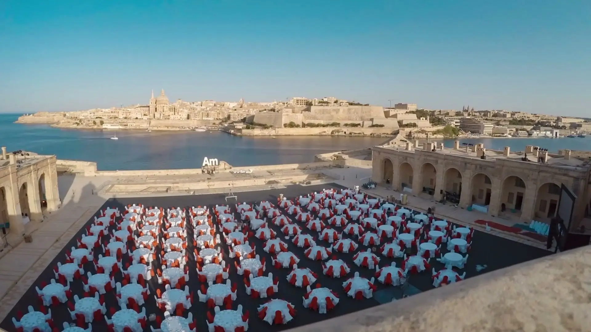 Fort Manoel's parade ground laid with rows of tables in red and white, Valletta across the harbour