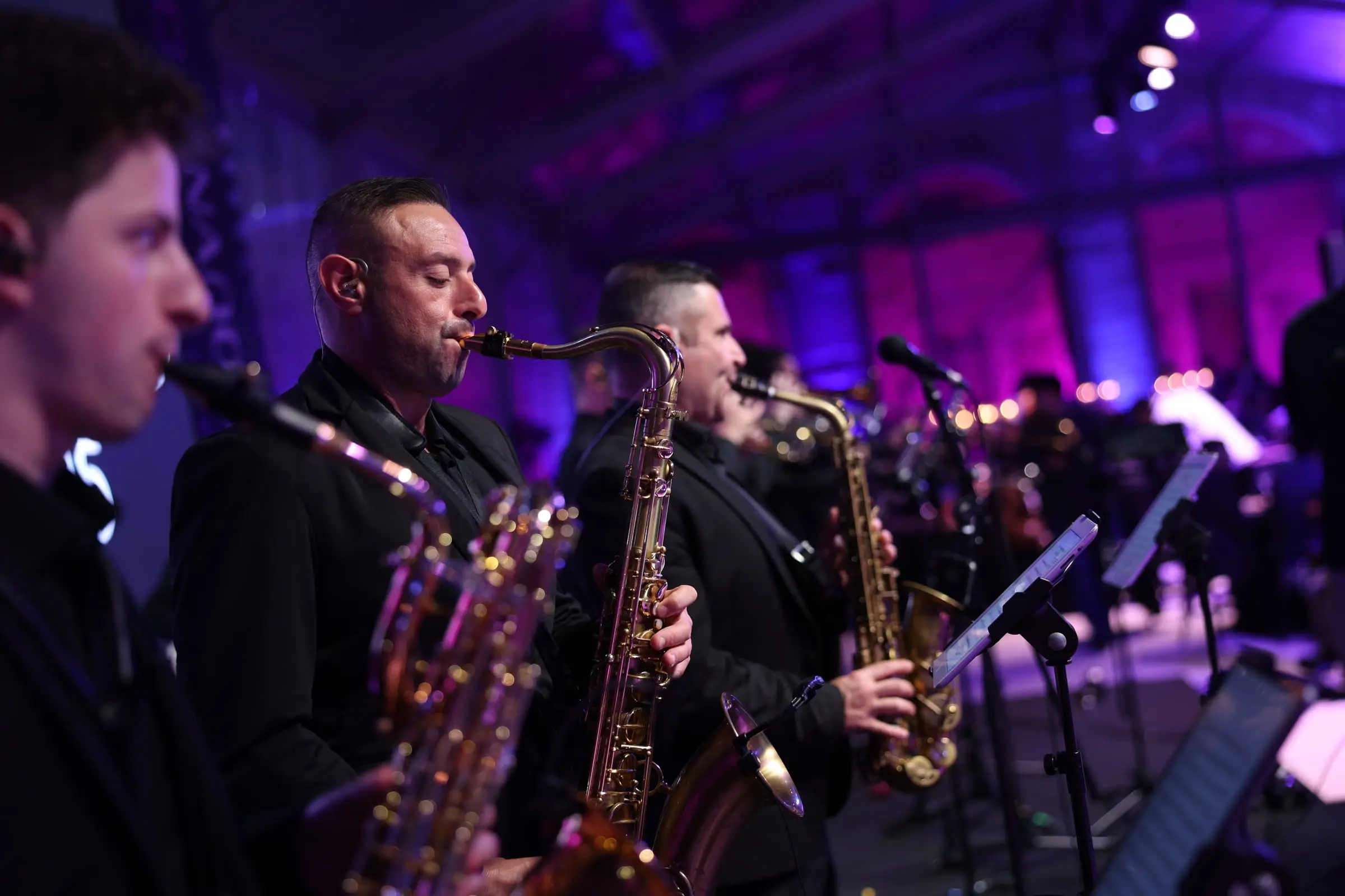 Saxophonists playing under purple light at the gala, their music on tablets on the stands