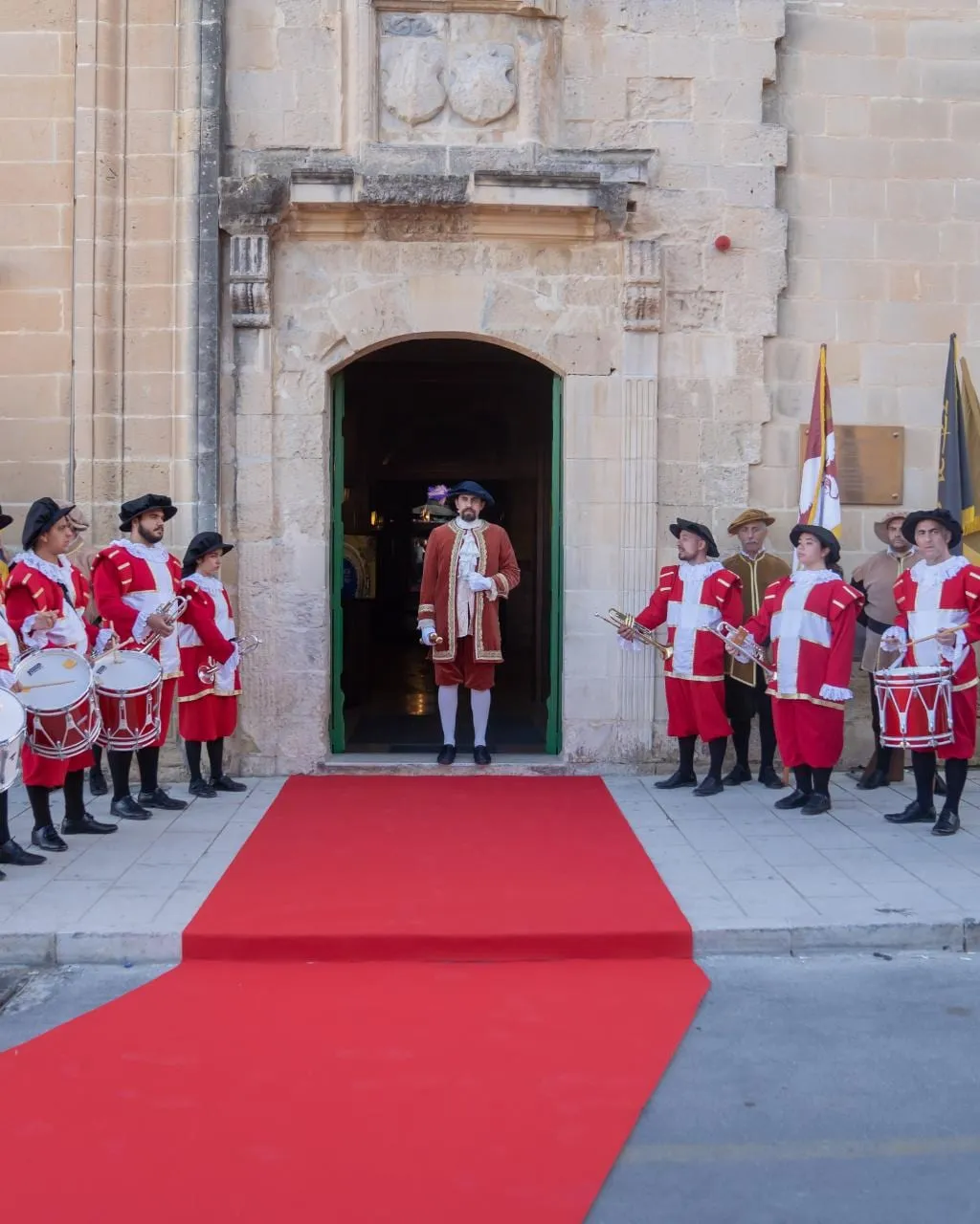 Costumed drummers and flag bearers lining a red carpet at the entrance to the Sacra Infermeria