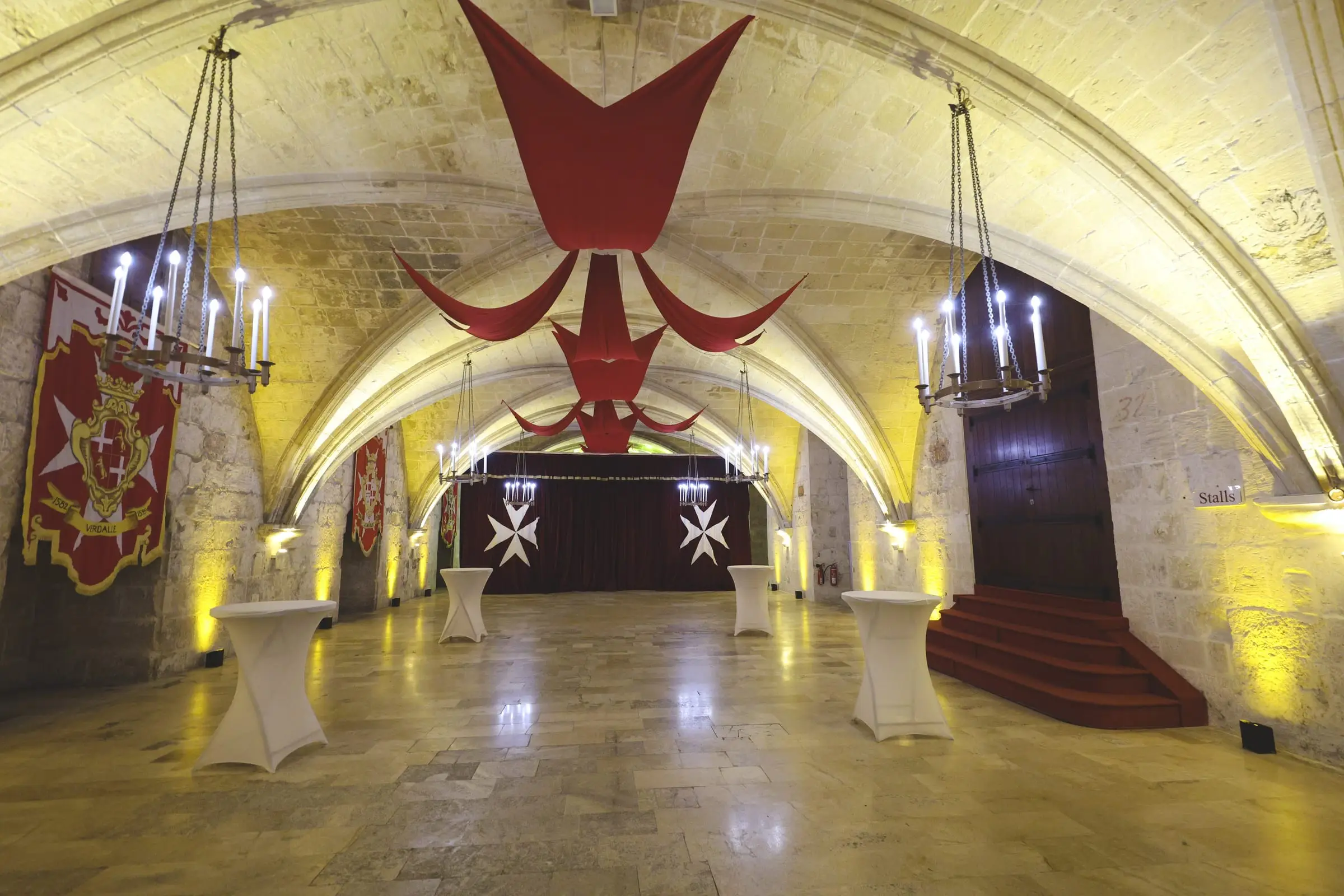 A vaulted stone hall at the Mediterranean Conference Centre hung with red drapes, candle chandeliers and the banners of the Order of St John