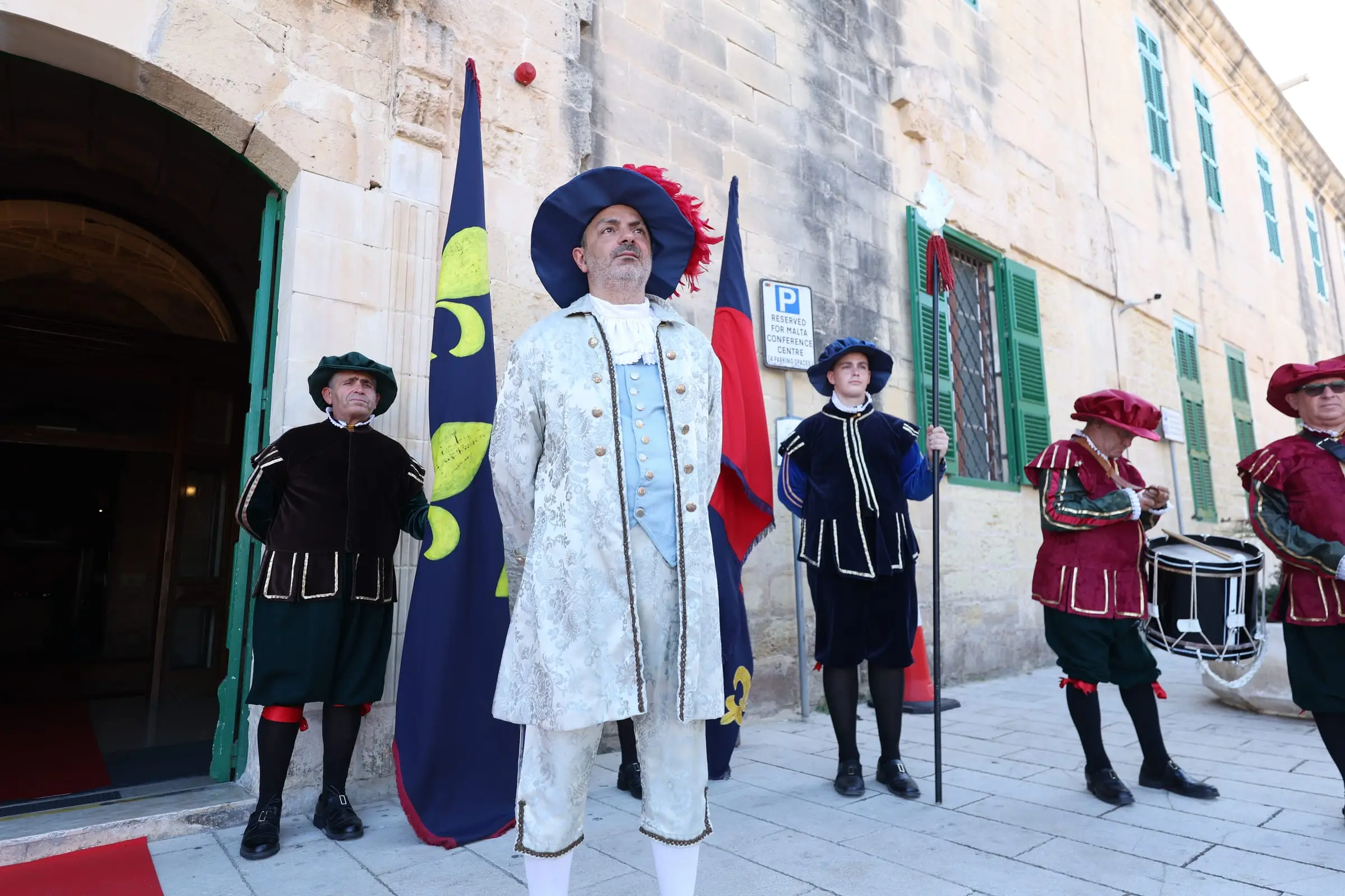 A costumed Grand Master of the Order flanked by halberdiers and a drummer at the Infermeria door