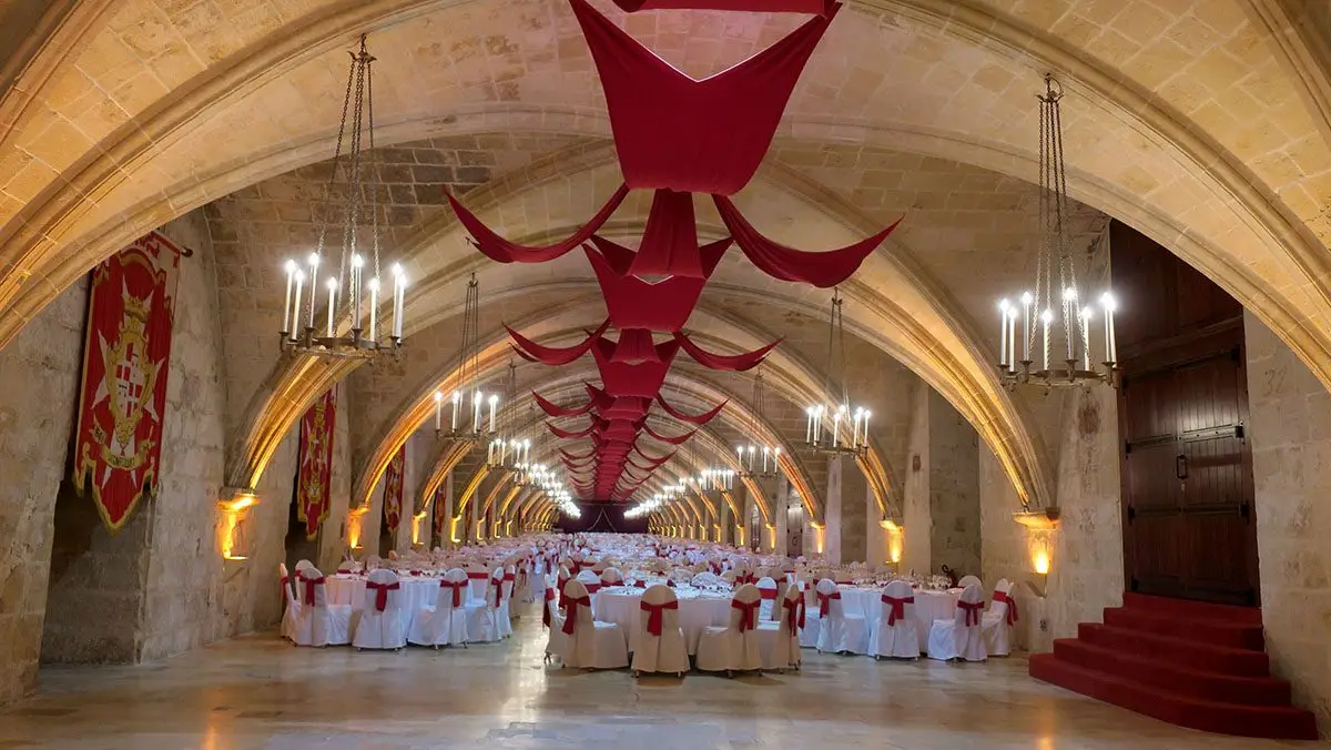 The vaulted hall of the Knights’ infirmary laid with round tables under red drapes and chandeliers
