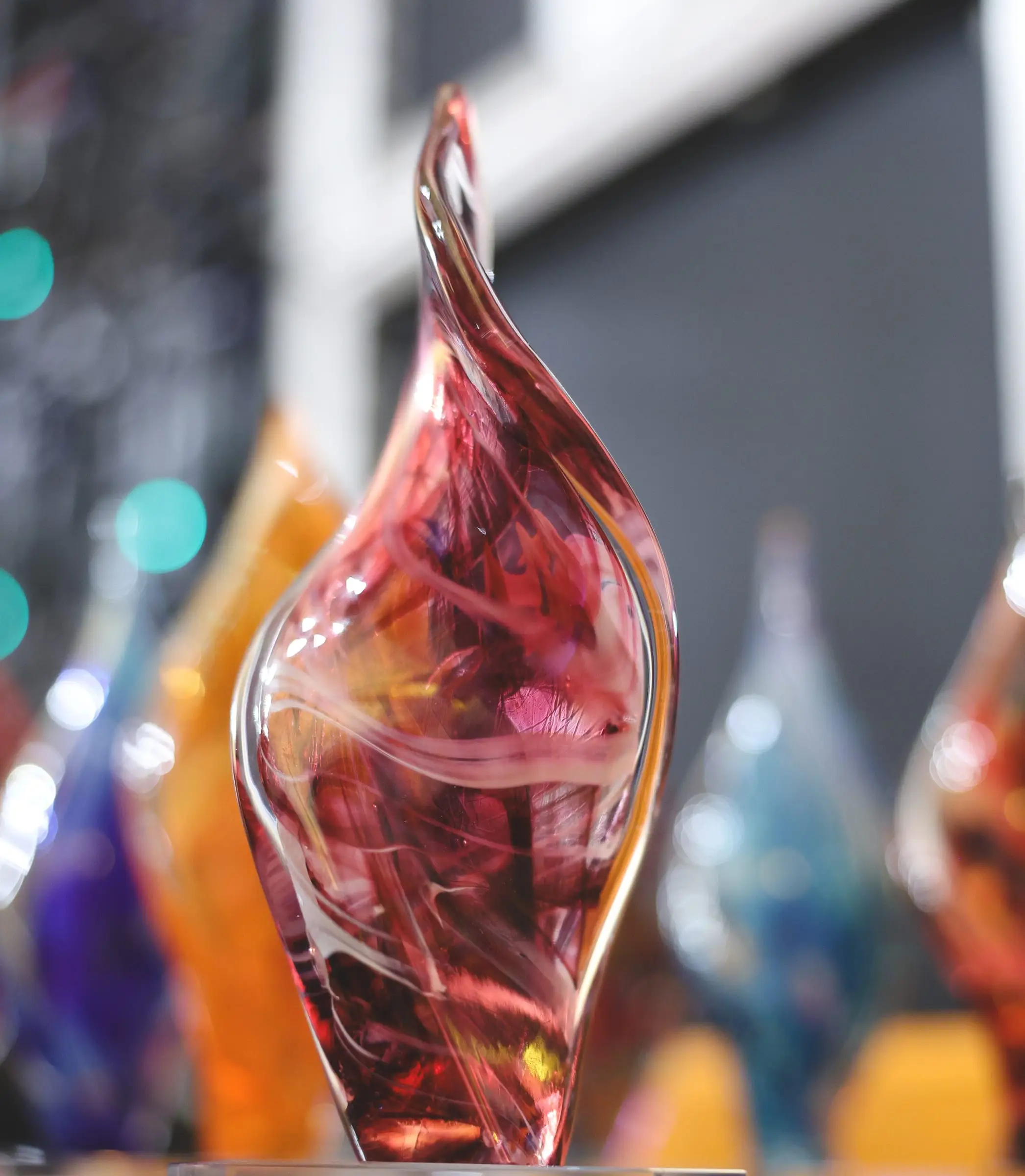 A hand-blown Mdina Glass trophy in swirling ruby and white, more trophies in amber and blue out of focus behind it