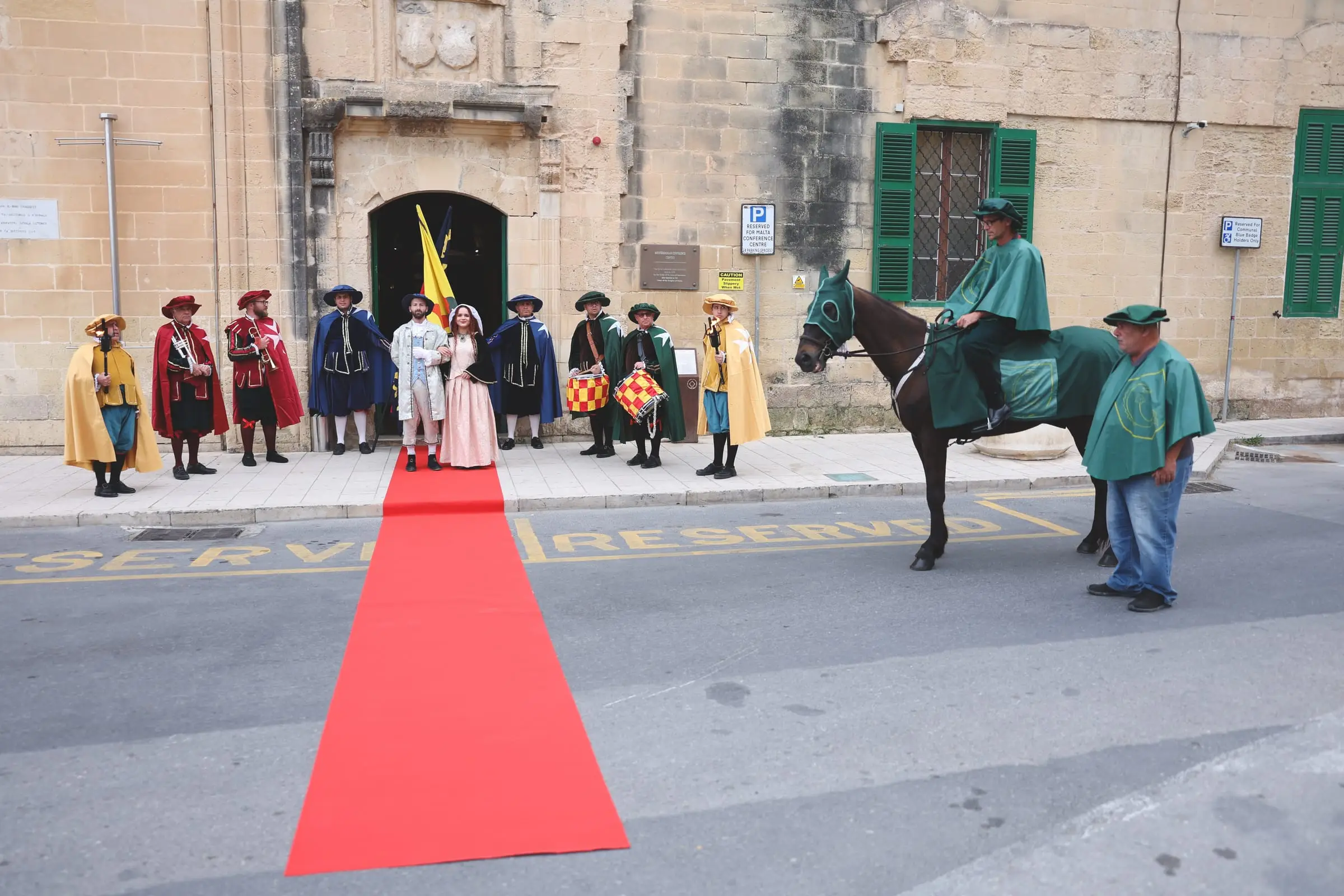 Torch bearers, trumpeters, drummers and a couple in period dress line the red carpet at the door of the conference centre, and a knight on horseback in green waits beside them