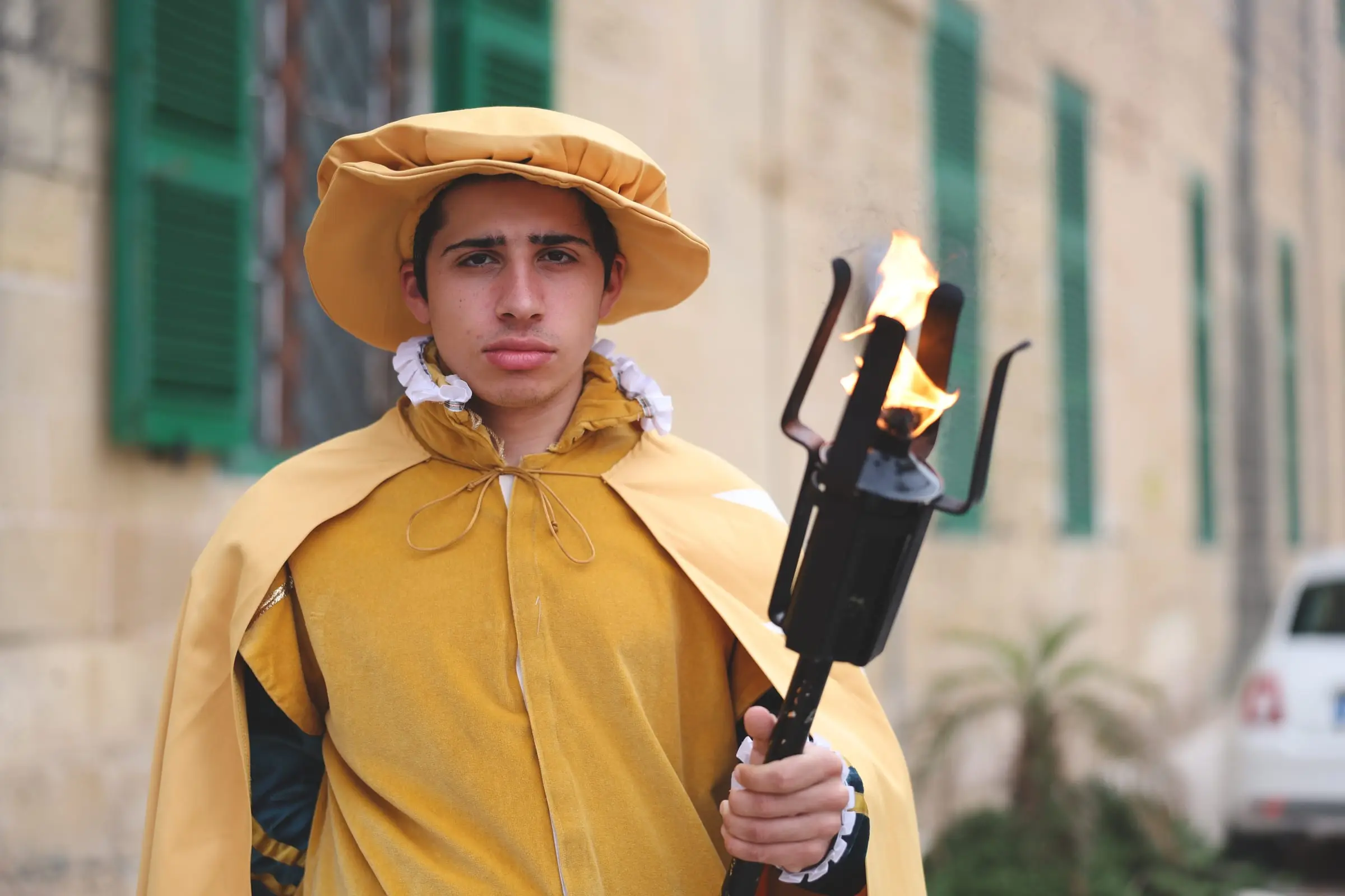 A young torch bearer in a mustard cape and velvet cap holds a burning torch outside the conference centre