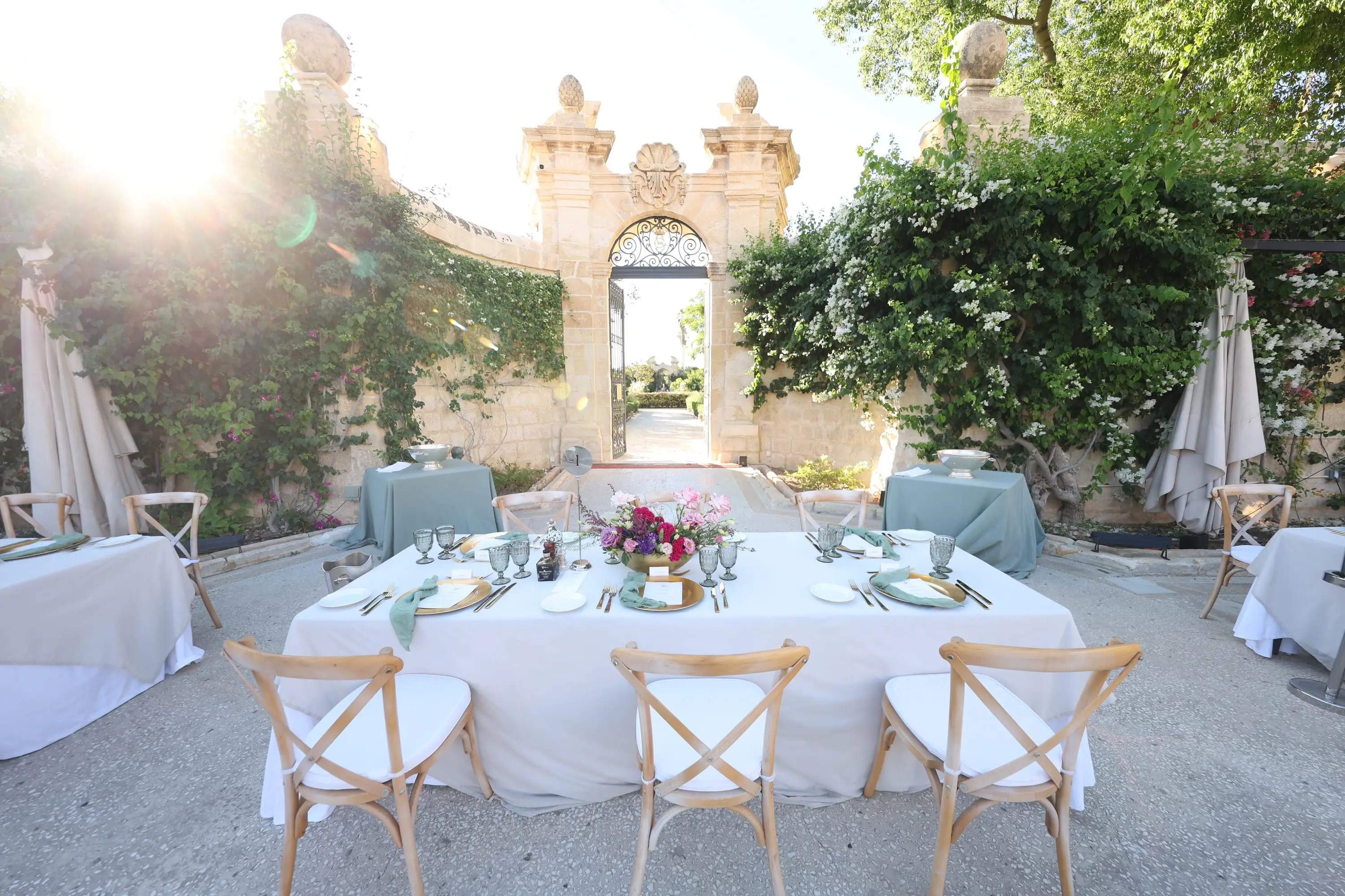 A golden-hour dinner table set before the baroque garden gate of Palazzo Parisio