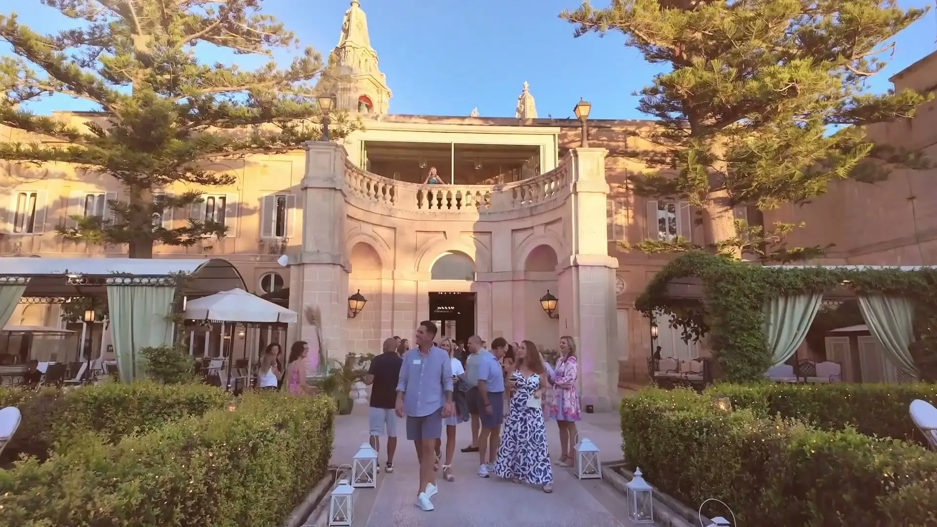 Guests walking through the formal garden of Palazzo Parisio towards the palace at golden hour