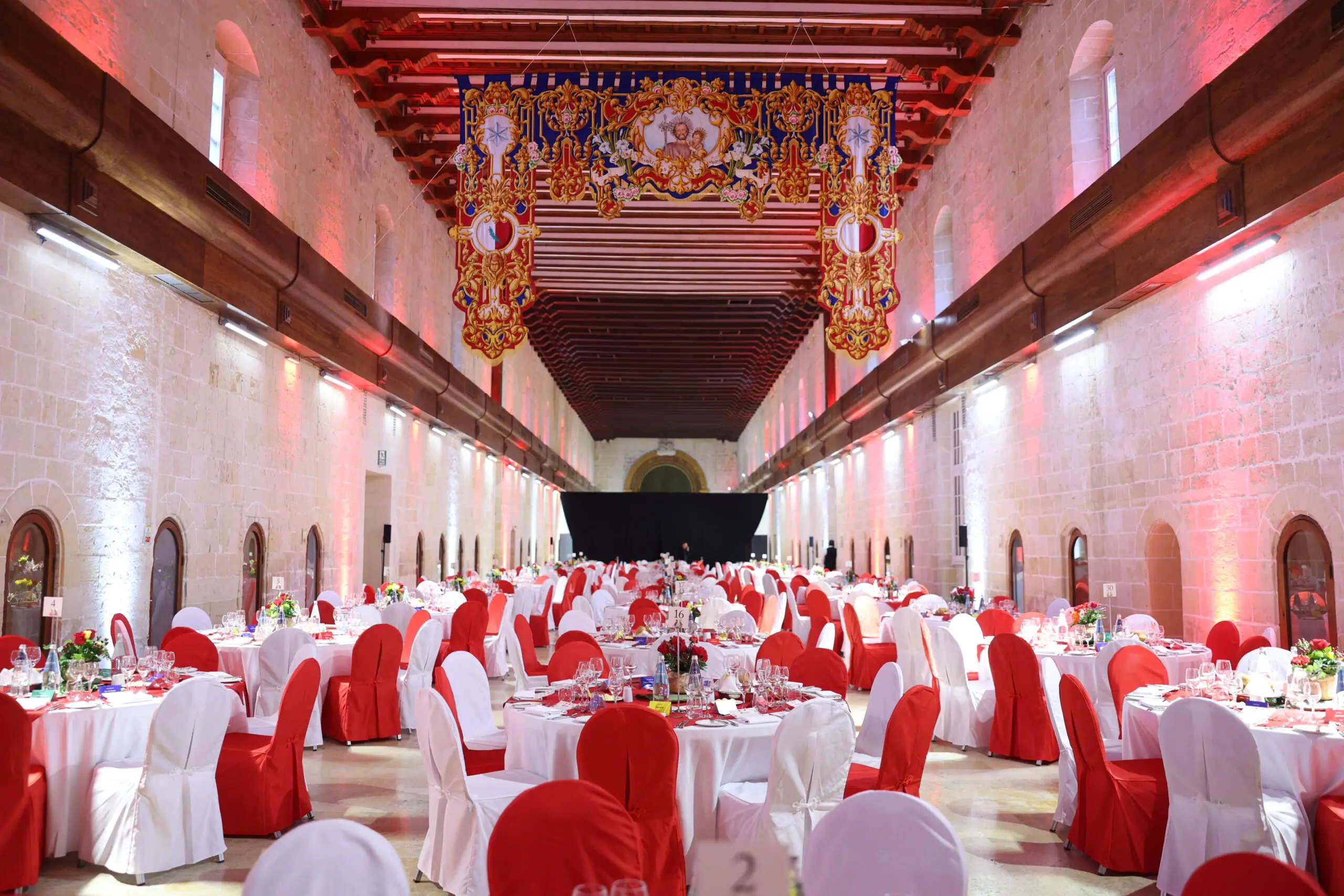 The long stone hall of the Sacra Infermeria laid with round tables in red and white, the Order's embroidered banners hanging from the timber ceiling