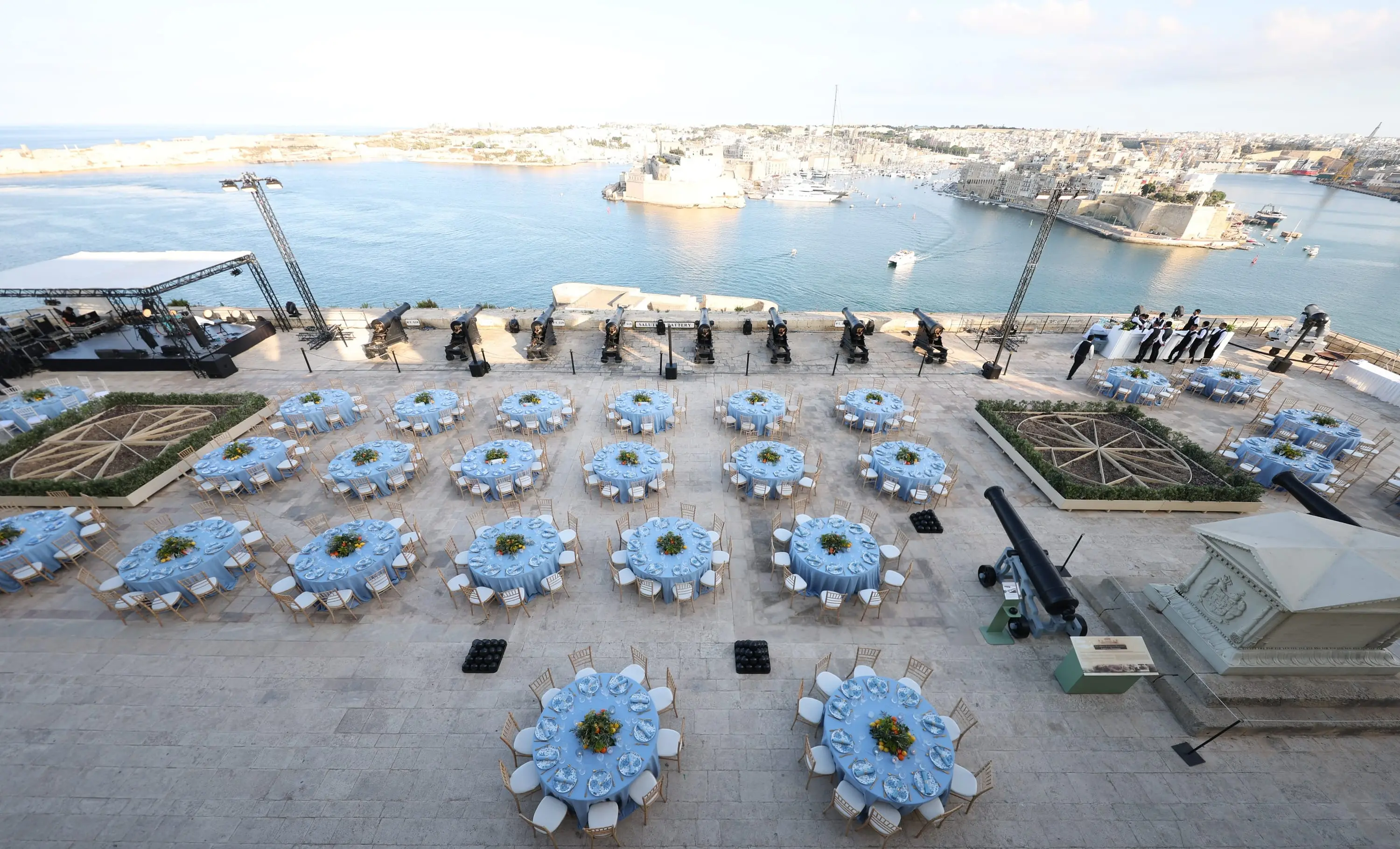 Round tables laid with blue cloths on the Saluting Battery in Valletta, its cannons in a row above the Grand Harbour, with Fort St Angelo and Birgu across the water