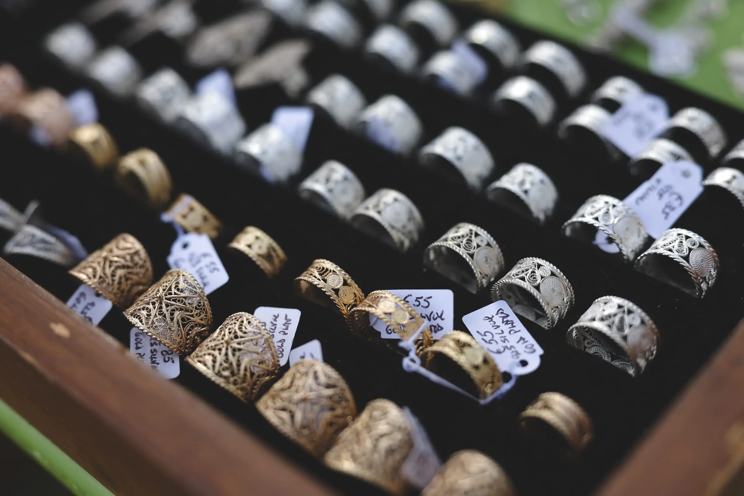 Silver and gold filigree rings in a wooden tray, hand-written price tags among them