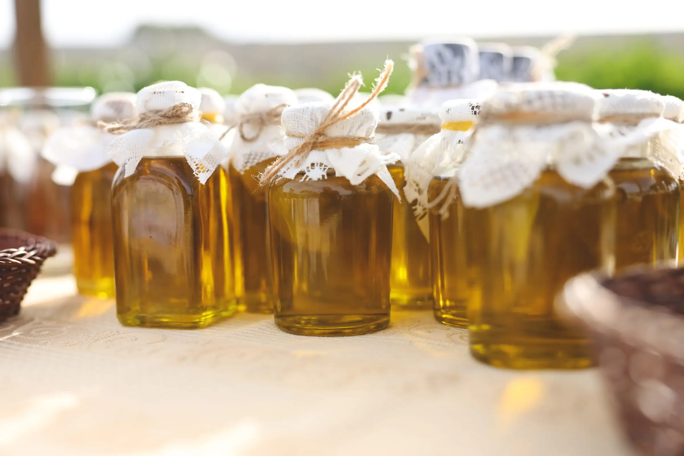 Jars of Maltese olive oil with lace covers tied with twine on a stall in the gardens