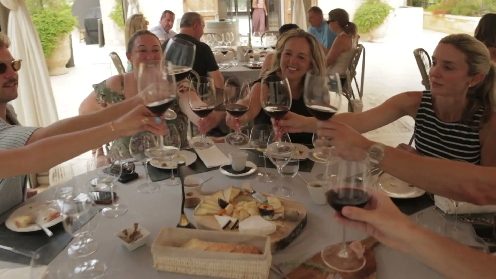 Guests raising glasses of red wine over a table of platters at a wine tasting
