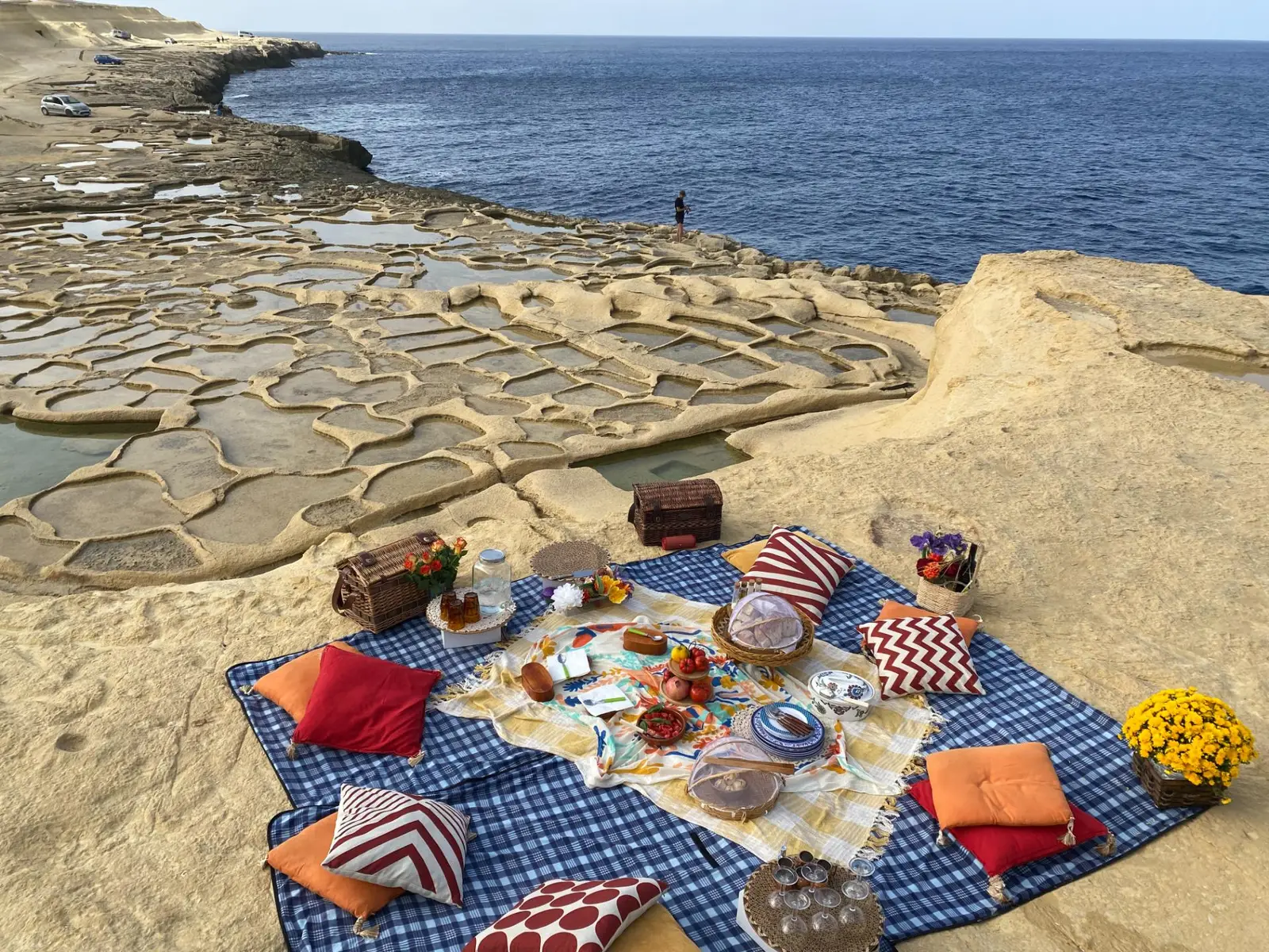 A picnic laid out on the rocks above the salt pans of Gozo, the sea beyond